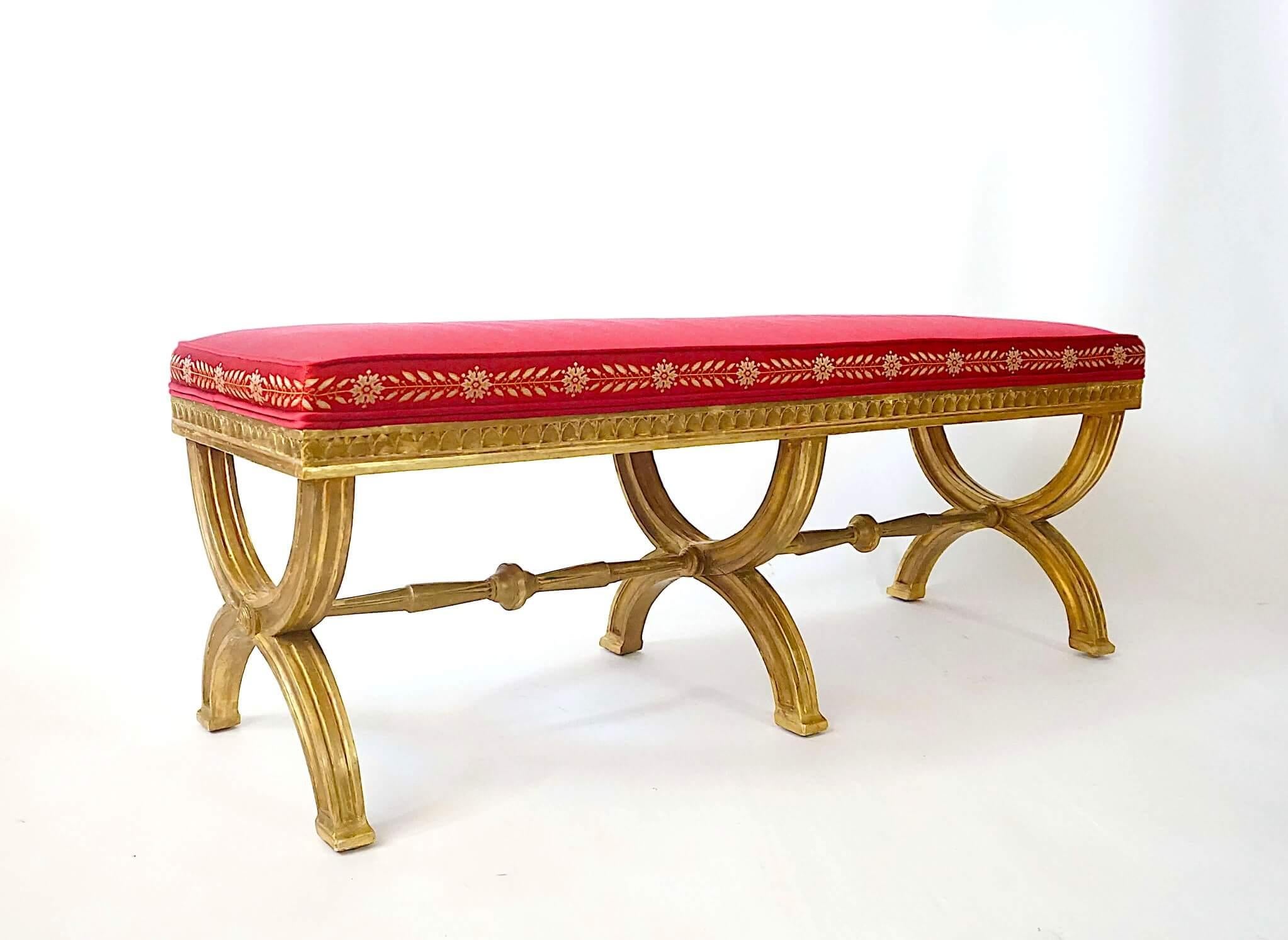 A rare and elegant circa 1805 Swedish late Gustavian period neoclassical long bench, the upholstered seat atop carved giltwood frame having tripartite curule leg supports connected by turned stretcher bars.  Height to top of seat rail is 15
