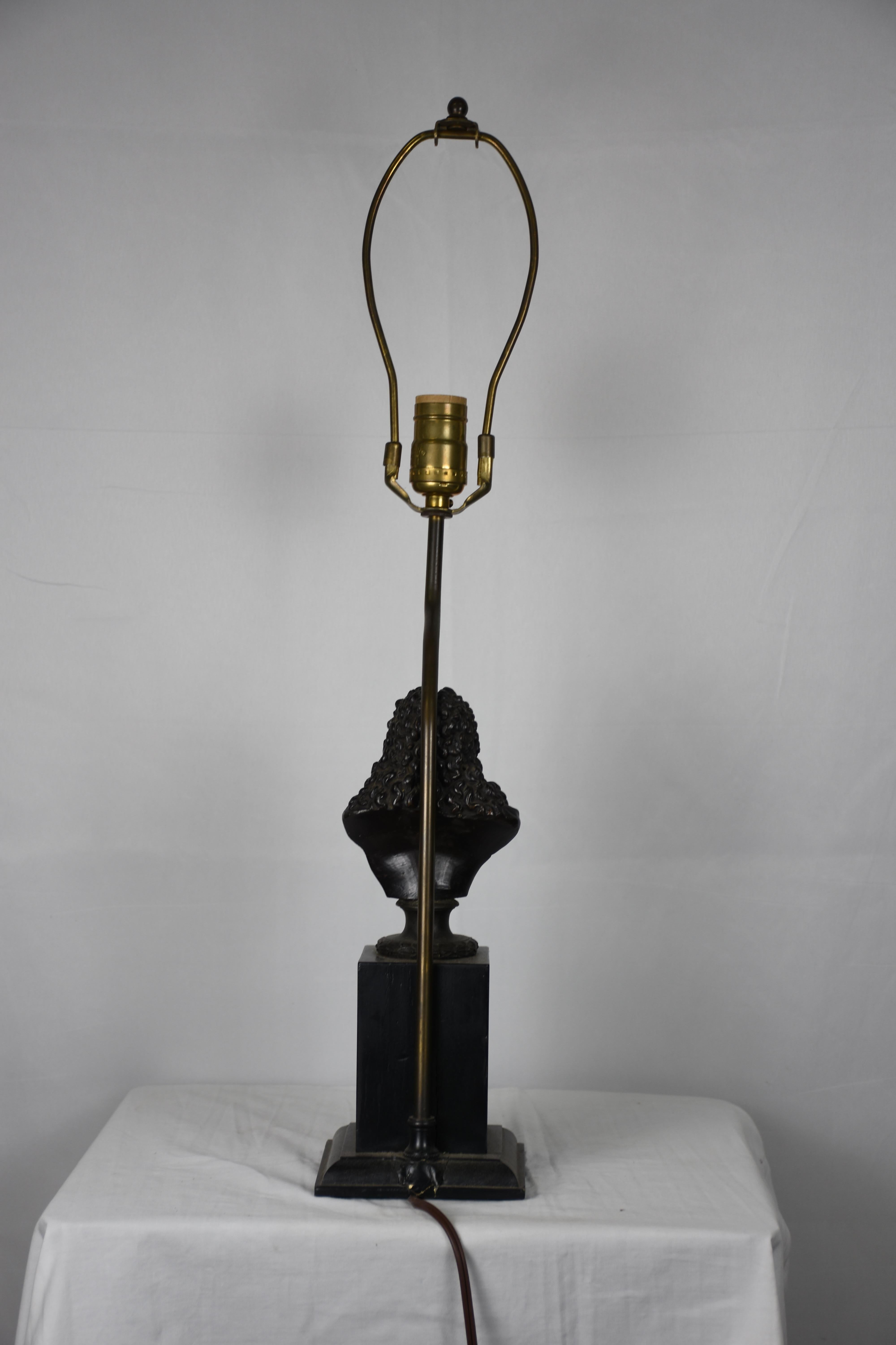 A sophisticated Neoclassical table lamp featuring a finely cast bust of a gentleman in period attire, mounted on a stepped plinth base. The bust, rendered in a dark patinated finish evocative of bronze, showcases intricate detailing in the hair,