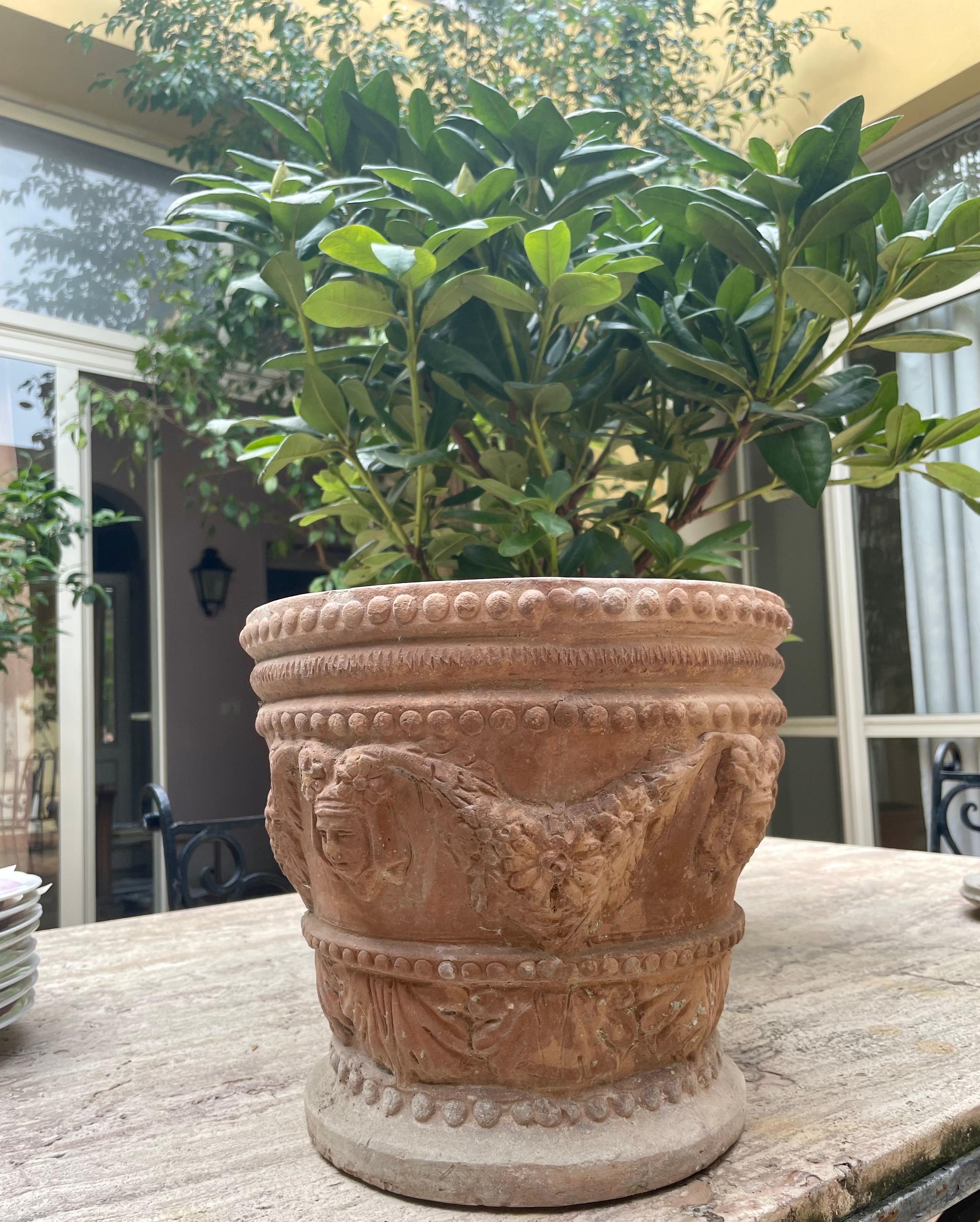 Neoclassical terracotta planter. Italian neoclassical style cachepot in terracotta with floral garlands strung from masks with large paired beaded banding to top and base. Crack to one side at top but physically sound and does not detract from