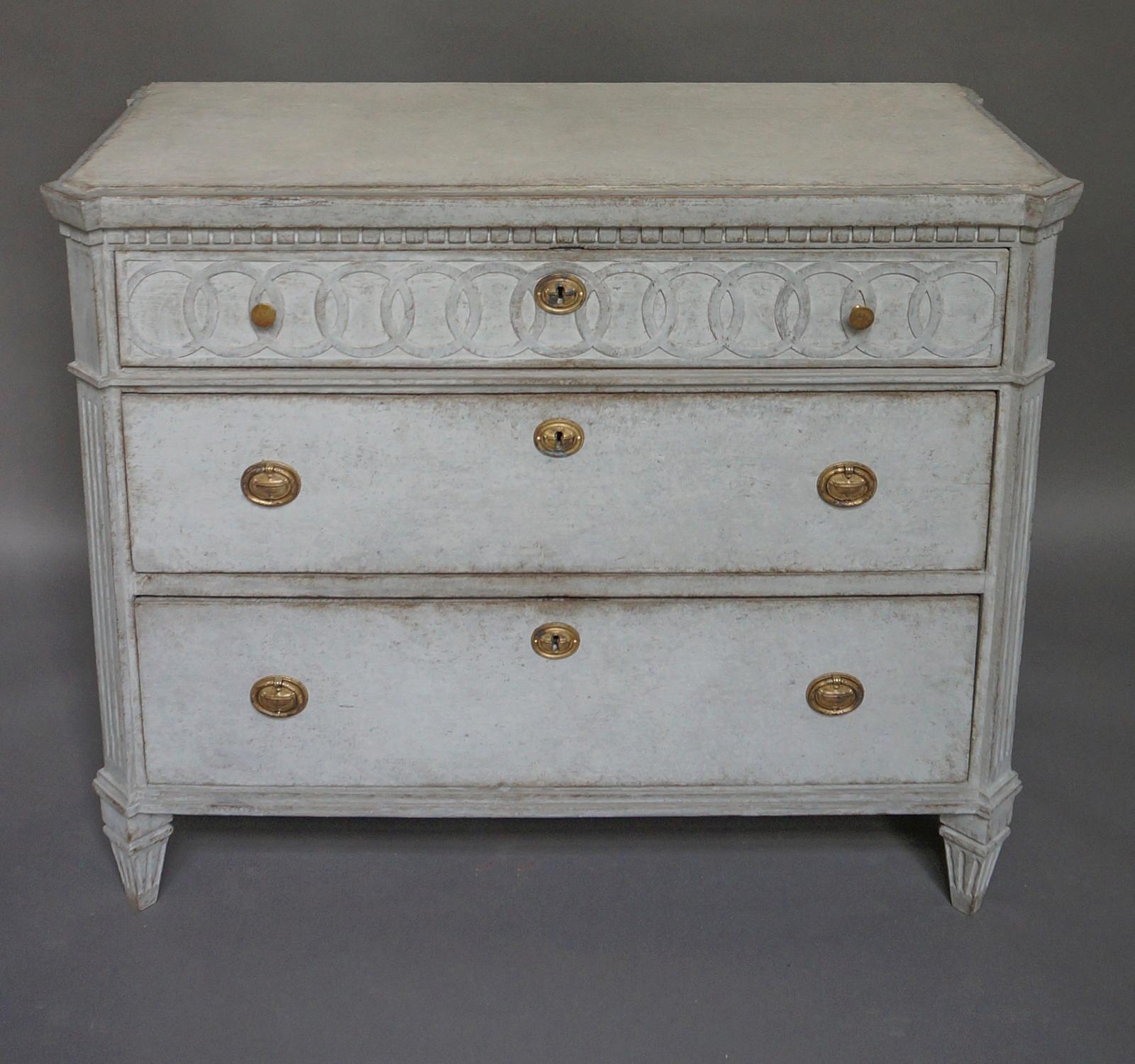 Neoclassical chest of drawers, Sweden circa 1860, with a panel of raised interlocking rings on the top drawer. Shaped top and chamfered corners with reeded detail over tapering square feet. Brass hardware of the period.