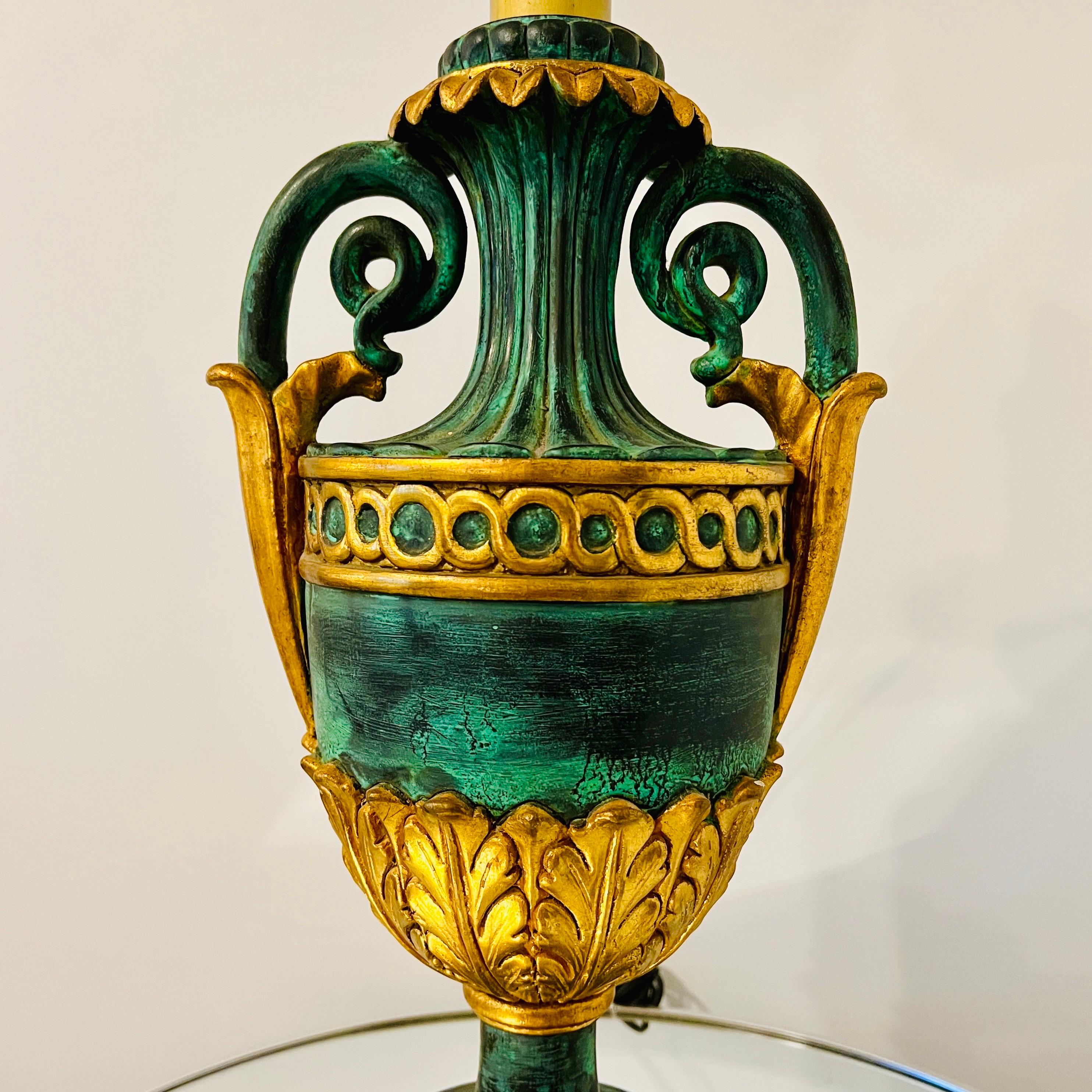 Neoclassical urn lamp in giltwood with hand-painted verdigris faux finish. Features highly stylized hand-carved designs with fluted details, scrolled handles,   gilded laurel leaf accents ,and gold circles.  Base measures 7.5