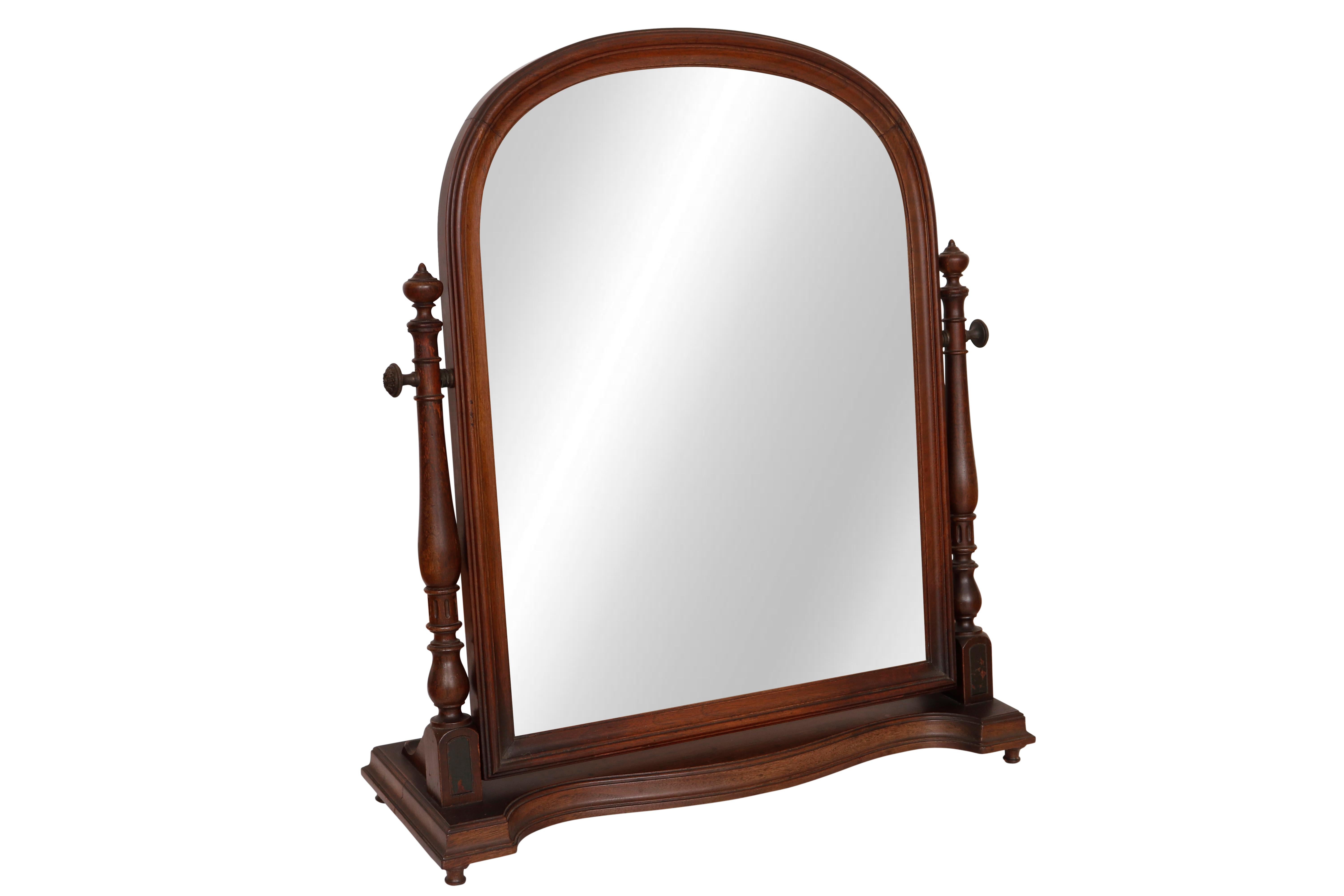 A neoclassical vanity mirror. An arched mirror set in a beveled wooden frame is supported with two turned posts. Each post is topped with an acorn finial and secured to the base with a curved bracket. The base is decorated with a serpentine curved
