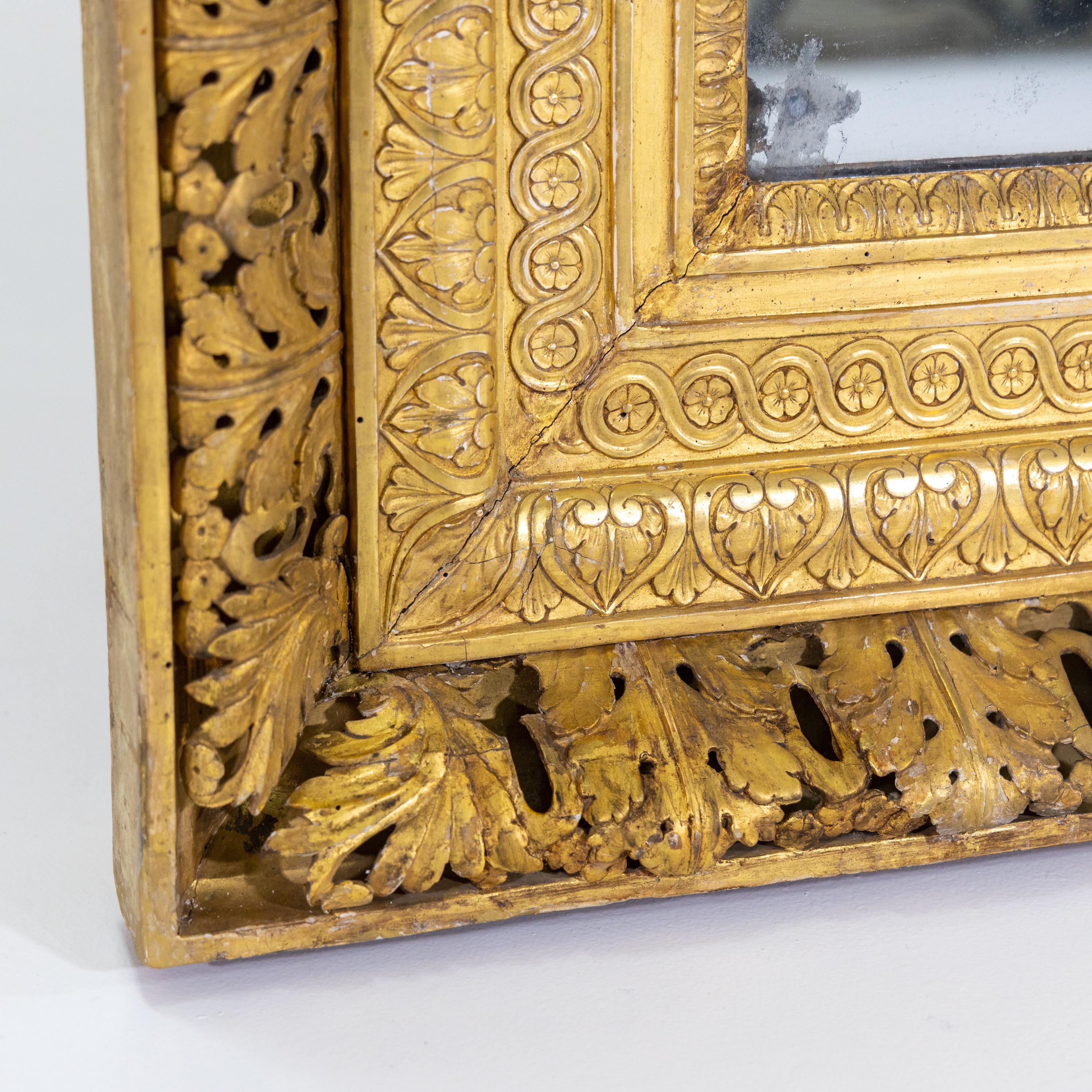 Wall mirror in a stuccoed and gold-patinated frame with openwork acanthus leaves, cymatium friezes and coin bands. The mirror glass has been renewed.
 
