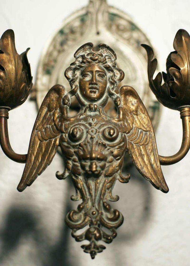 Etruscan style brass wall sconce. This cherubic centerpiece is flanked by two floral scalloped arms and is cast with a brass finish.