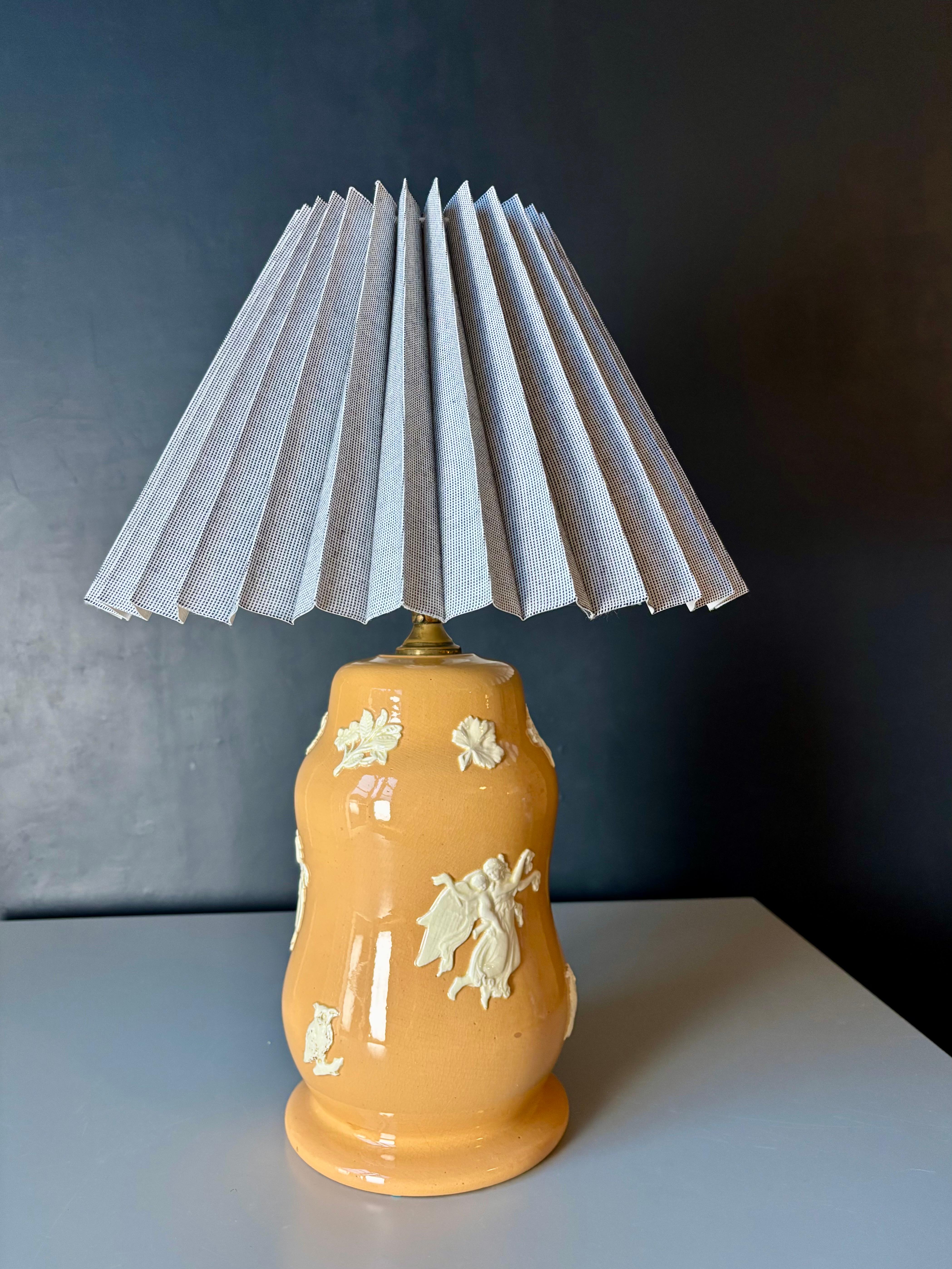 Honey yellow glazed soft shaped neoclassical Wedgwood Jasperware style table lamp with silky white molded relief decorations depicting human figures, birds and floral ornaments. Danish handmade pleated shade in gray and white - replaced with a white