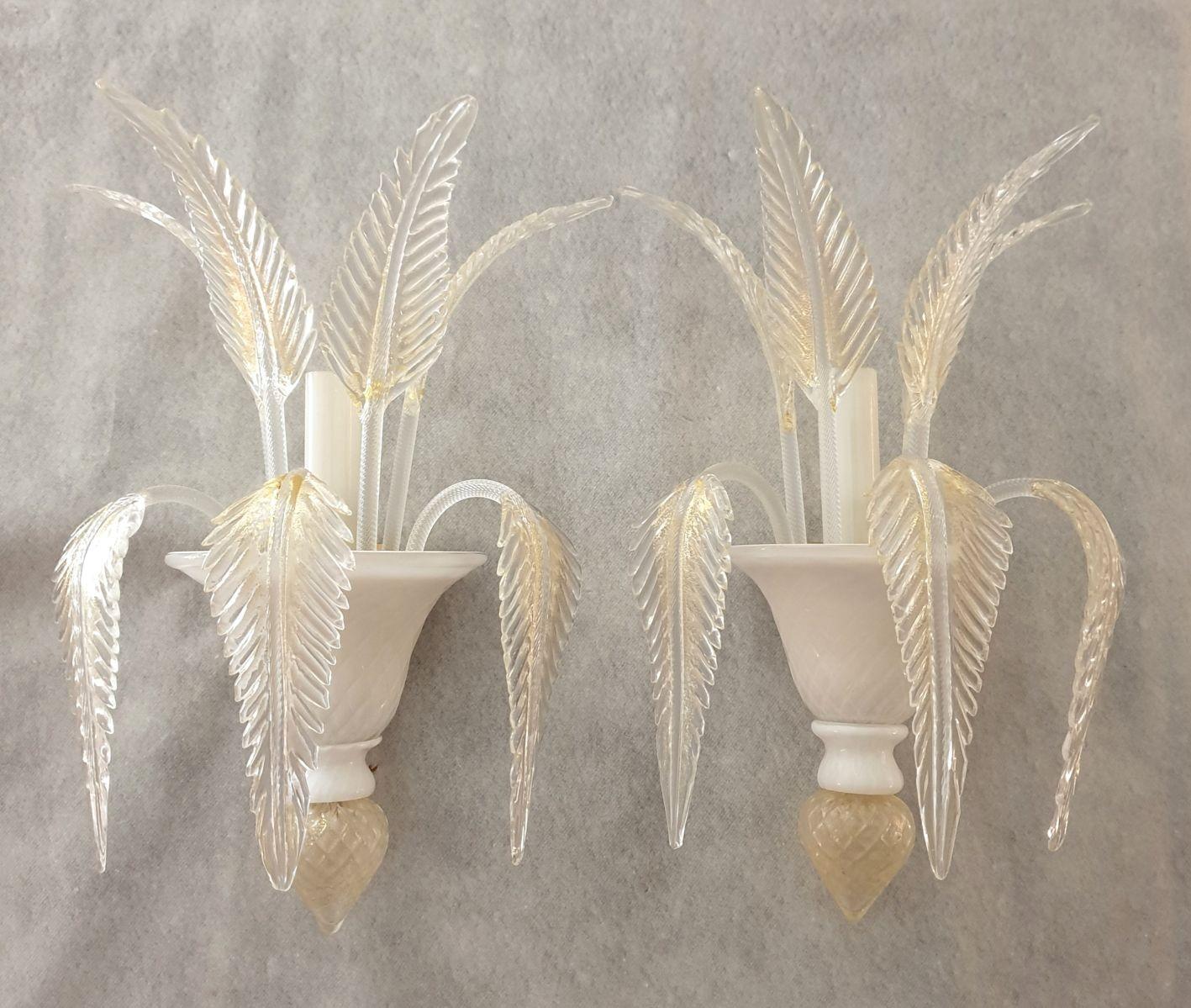 Pair of Neoclassical style Murano glass wall sconces, attributed to Venini, Italy 1970s.
The Mid Century sconces are made of hand blown Murano glass.
They have a milk white bottom vase and six delicate clear and gold leaves.
A glass white tube is