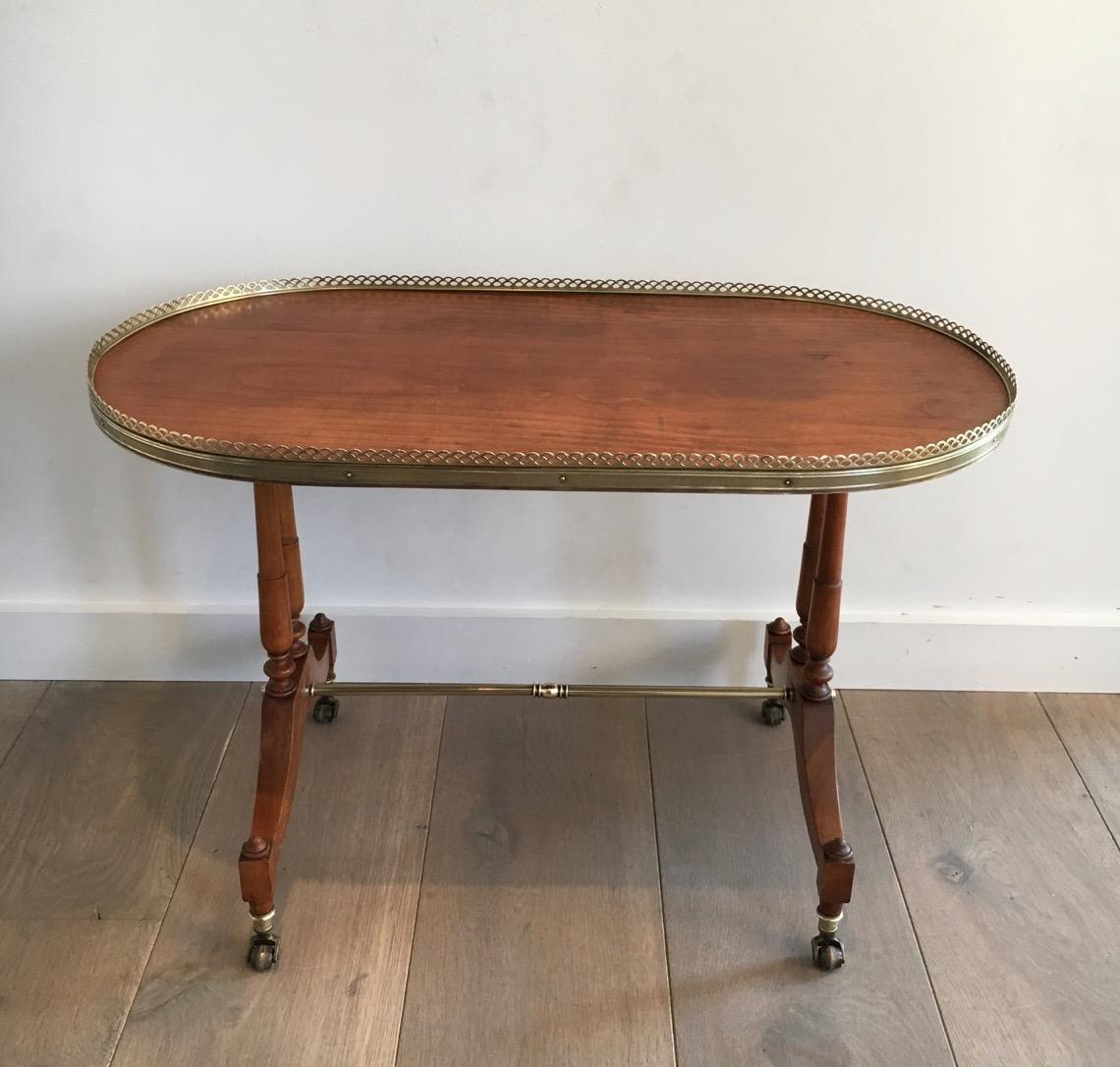 This neoclassical oval coffee table is made of cherrywood. The top of the table is surrounded by a nice brass gallery. The cocktail table also has a nice brass stretcher as well as brass casters. This is a French work, circa 1940.