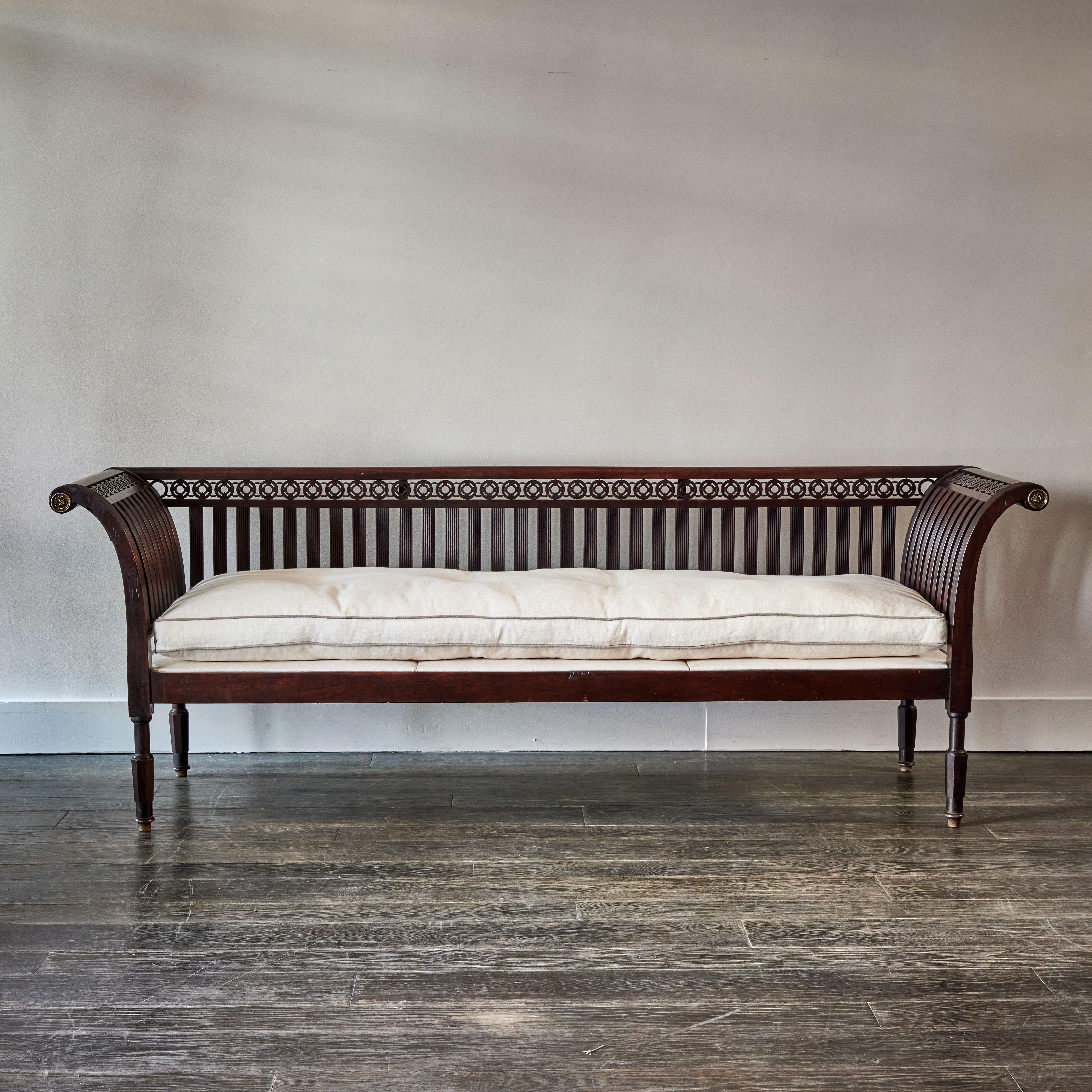 Early 19th-century Empire style wood bench or settee. A wonderful example of Continental Neoclassicism, the piece features a slatted, wonderfully detailed hand-carved wooden back and armrest in a rich coffee hue, and a new, custom tufted linen