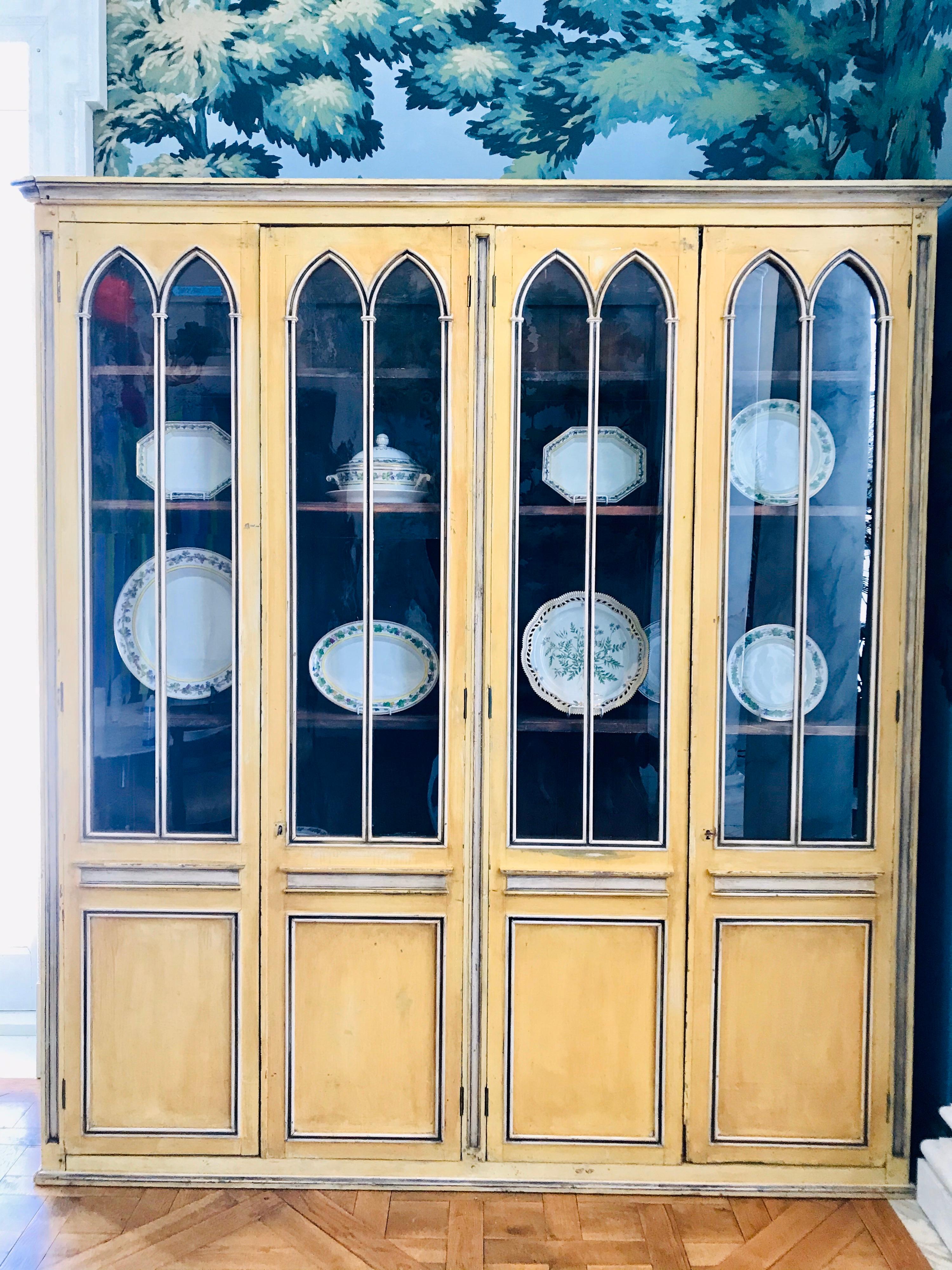 Beautiful Neo-Gothic style French Country four door bookcase, hand painted in yellow and grey tones with accents of deep blue.
It was manufactured in the 1980s using old materials and looks convincingly to be from 1840.