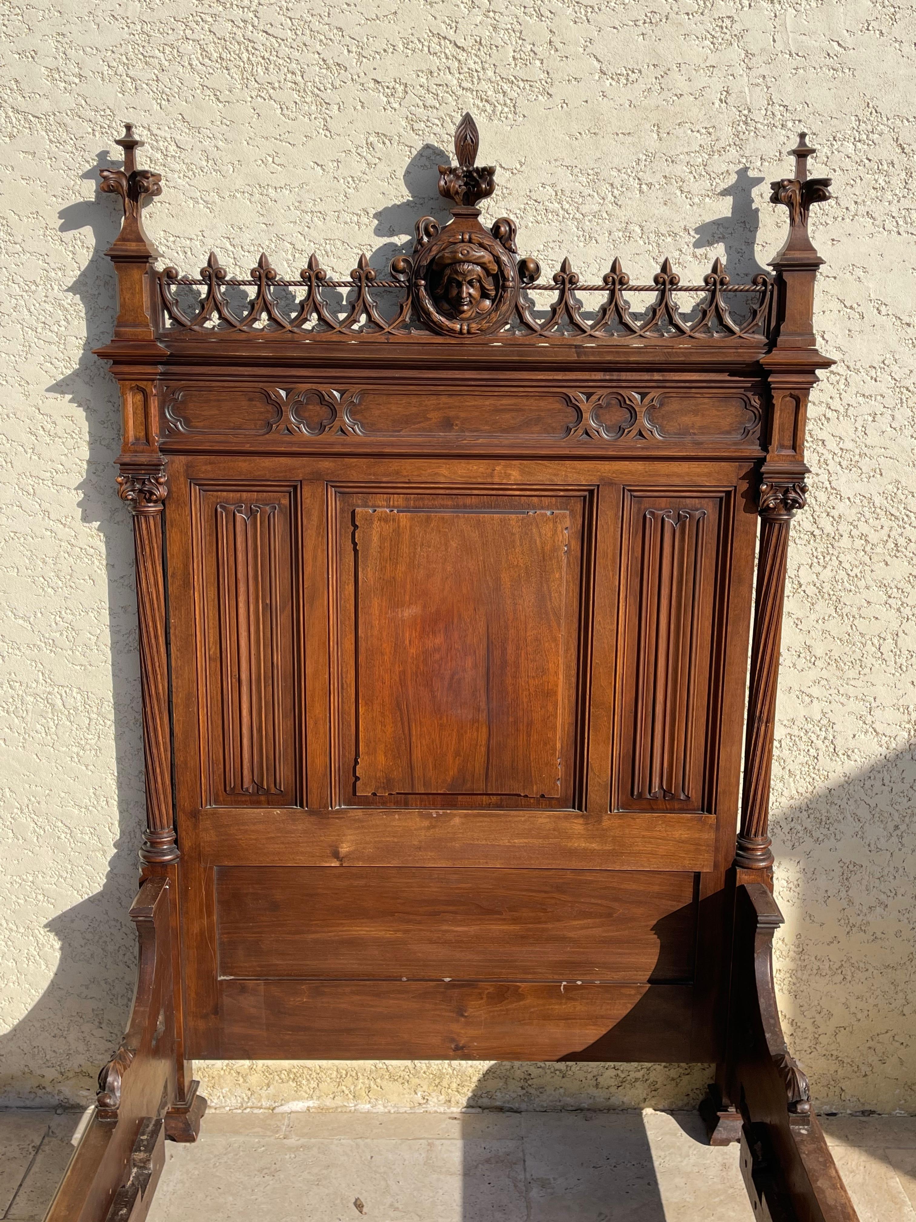 Neo-Gothic style single bed in walnut richly carved with napkin folds, warheads, arrowheads, cabbage leaves. Pediment and footboard featuring a macaroon with the face of a man inside. This bed is in very good condition. This bed can be combined with