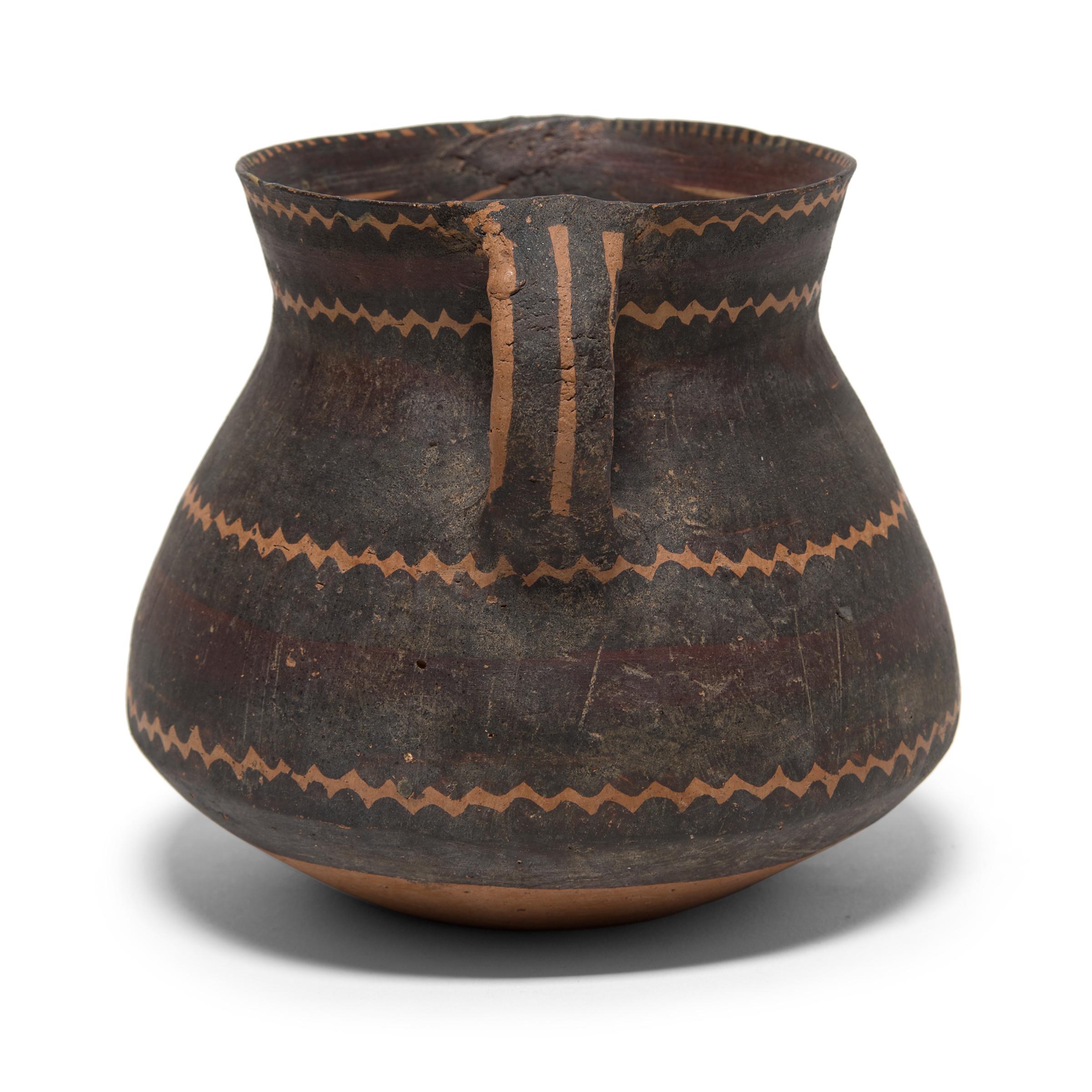 This petite ceramic jar is a fine example of late Neolithic pottery of the Yangshao culture. Distinguished by the red-orange earthenware and squat form, the jar is decorated with a geometric saw-tooth pattern and criss-crossed lines around the lip.