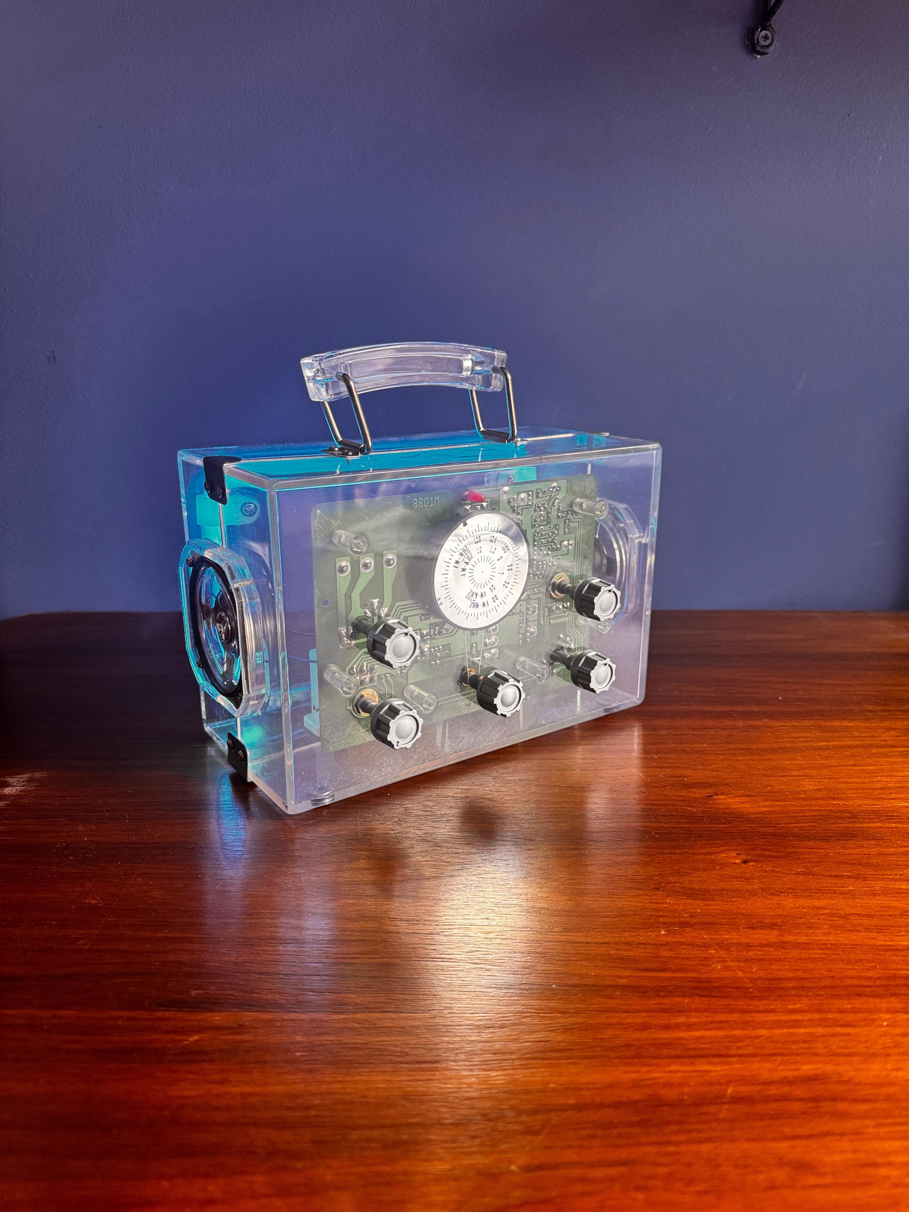 Ce boîtier radio Neon Cube, fabriqué en 1978, est un exemple frappant de design électronique de la fin du XXe siècle qui fusionne l'esthétique ludique et la transparence technique. Logé dans un cube en acrylique entièrement transparent, il révèle