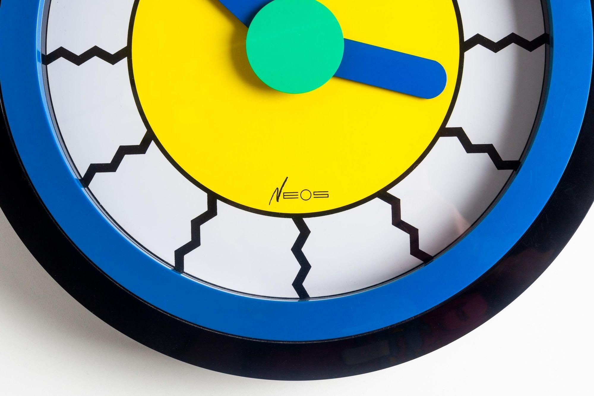 A bright, multicolored postmodern wall clock with blue and green hands designed by Nathalie du Pasquier and George Sowden for Neos of Lorenz in the late 1980s. Co-founders of the Memphis Group, du Pasquier and Sowden designed numerous clocks for