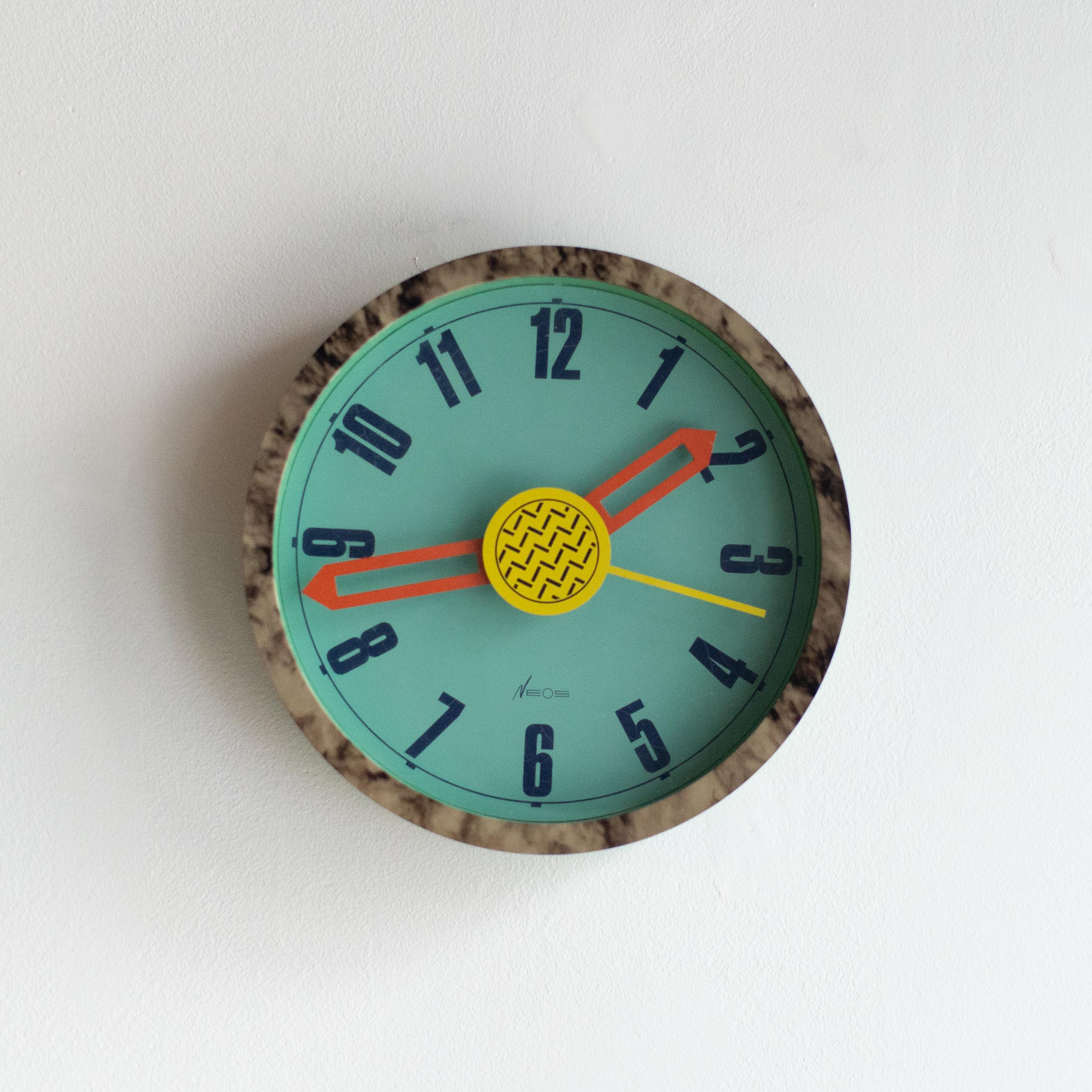 Neos clock designed by George Sowden and Nathalie du Pasquier in the 80s. Neos is the brand run by Lorenz clock company in Italy. They were designed a lot of clock and watch for this company in the 80s. 
Clocks are all Memphis style.

Working