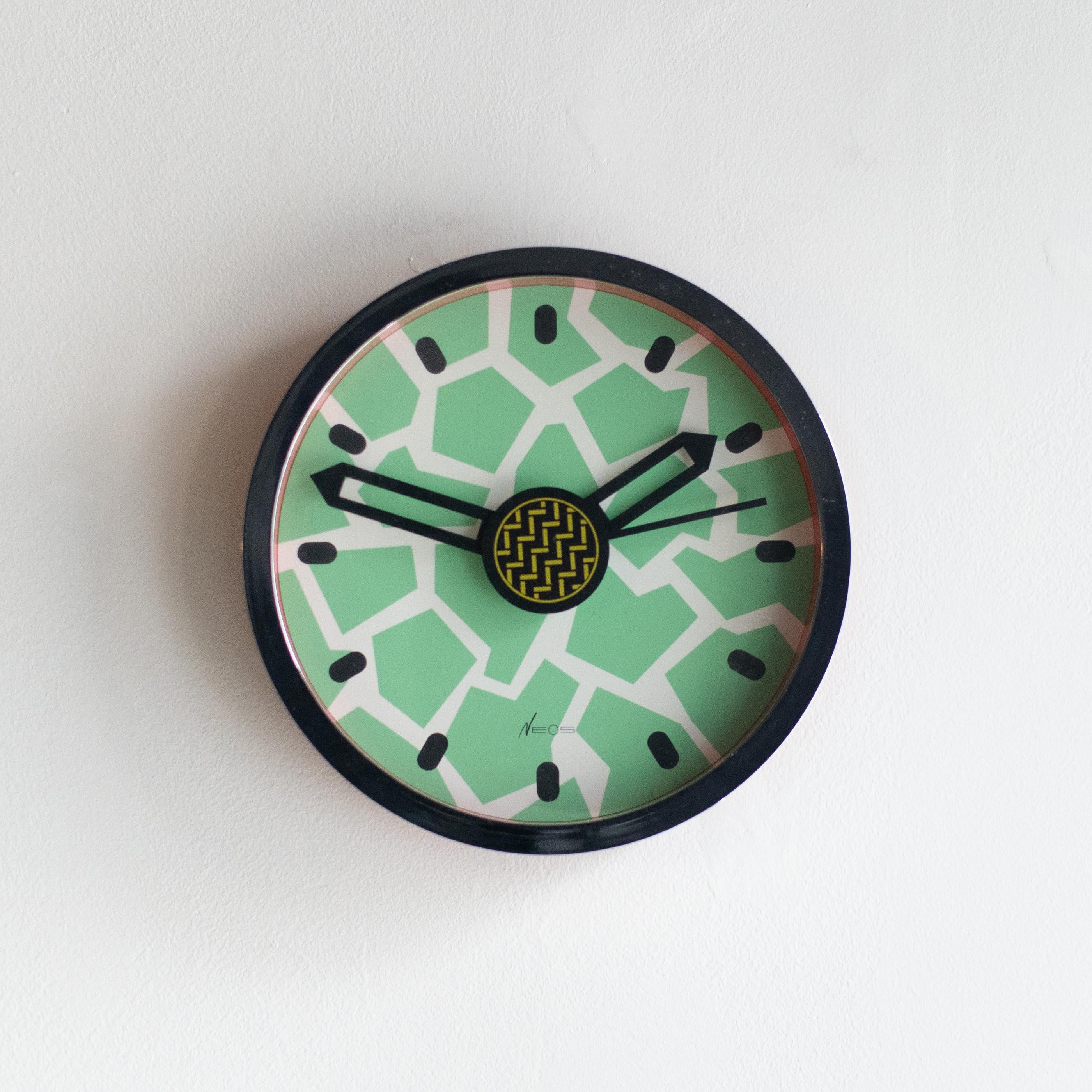 Neos clock designed by George Sowden and Nathalie du Pasquier in the 80s. Neos is the brand run by Lorenz clock company in Italy. They were designed a lot of clock and watch for this company in the 80s. 
Clocks are all Memphis style.

Working