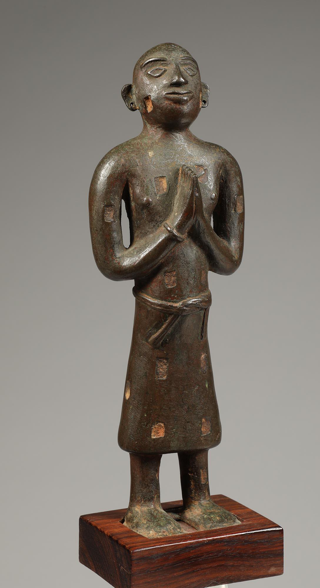 Old Nepal or India solid cast bronze standing namaste figure with hand clasped on chest. Sweet open eye expression and ears pierced for earrings (now missing). Series of rectangular openings that probably one held semi-precious stones or other metal