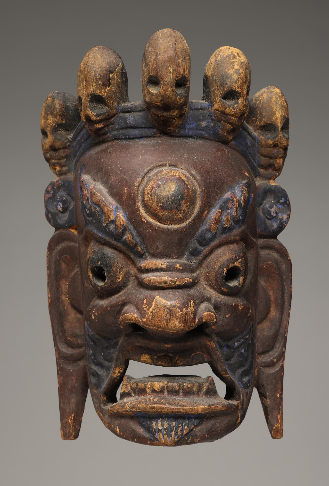 Masque de danse de petite taille en bois sculpté du Népal, à l'expression puissante, aux yeux et à la bouche ouverts avec des dents et des crocs sculptés, représentant le Mahakala bouddhiste, le chasseur de démons. Le sommet de la tête comporte 5