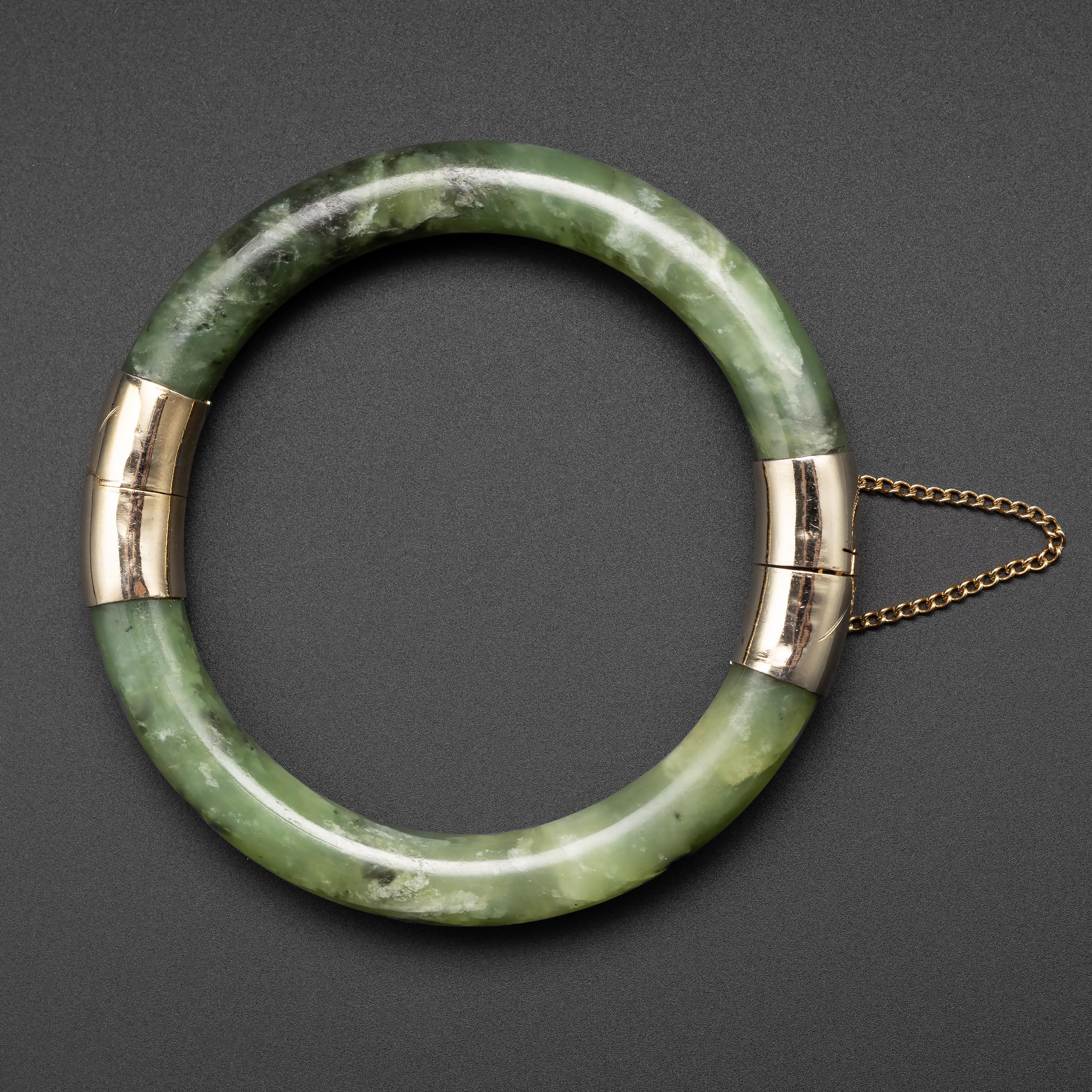 This Midcentury (circa 1970s) nephrite jade bangle is highly translucent and displays beautiful natural stone grain. The interior diameter is approximately 61.51mm, but because the bangle is hinged, it will fit larger wrists. A hinged bangle is