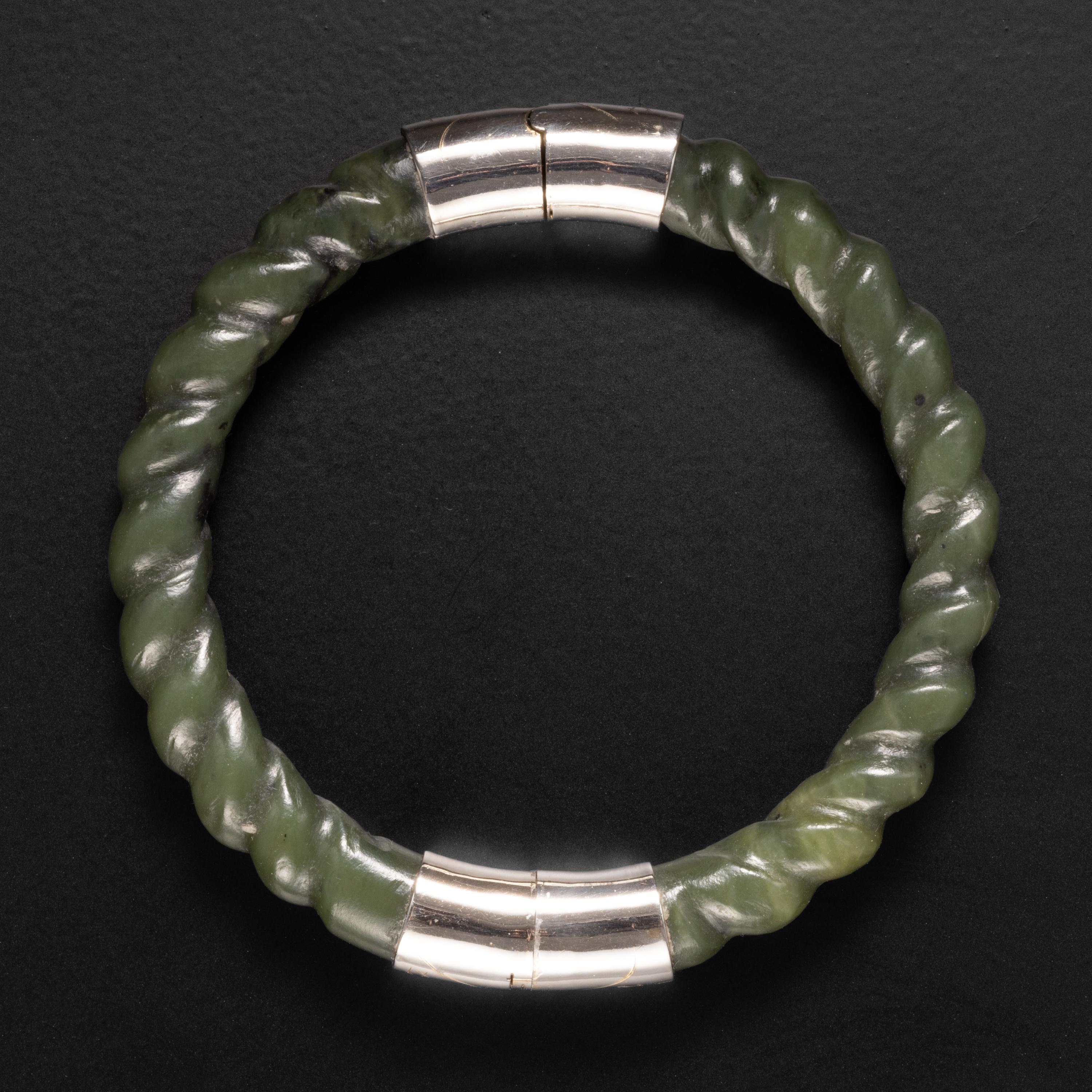 This deep green nephrite jade bangle was hand-carved in the early 1950s to resemble twisted rope. It displays the pre-industrial revolution polish of that era, before electric tools and diamond polishing compounds were in wide usage in China. This