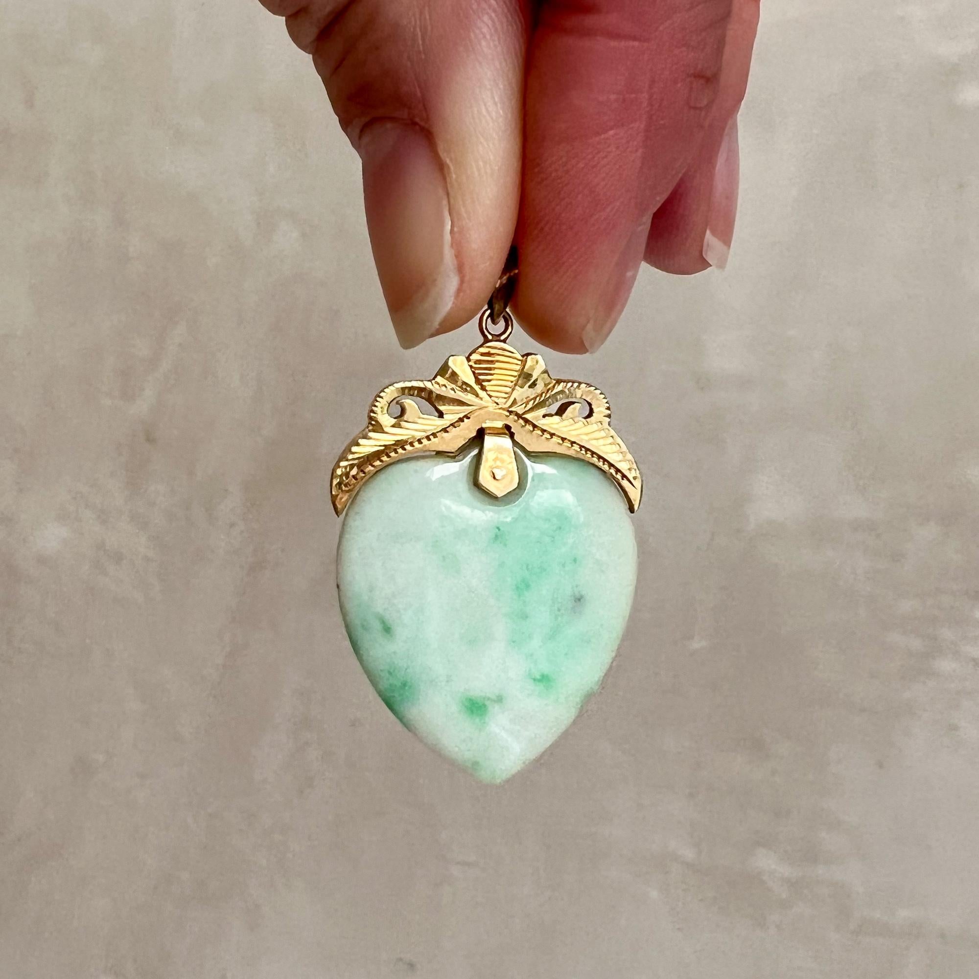 A nephrite jade heart pendant set with a 14 karat gold bail. The jade has a mottled and marbled white and green color, the opaque jade stone is beautifully polished and of high quality. The decorated gold frame above the jade heart is beautifully