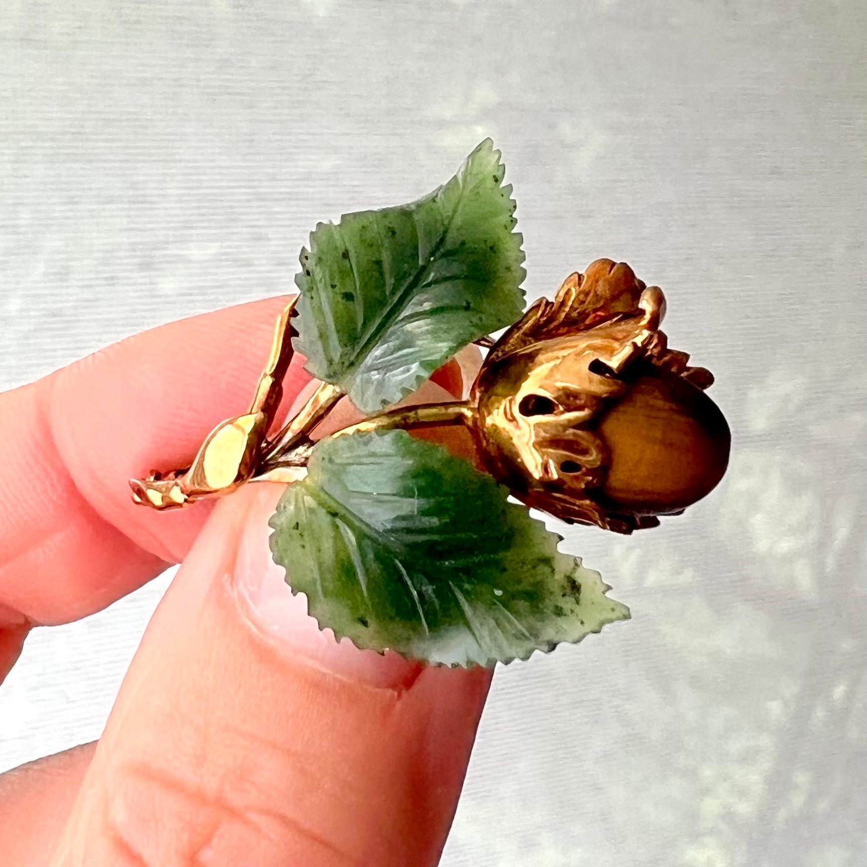 This is a  14 karat yellow gold branch brooch created with beautifully realistic leaves carved from nephrite and tiger's eye acorn inlaid in a mantle of gold. This naturalistic brooch is made in the shape of a freshly fallen branch with a brown