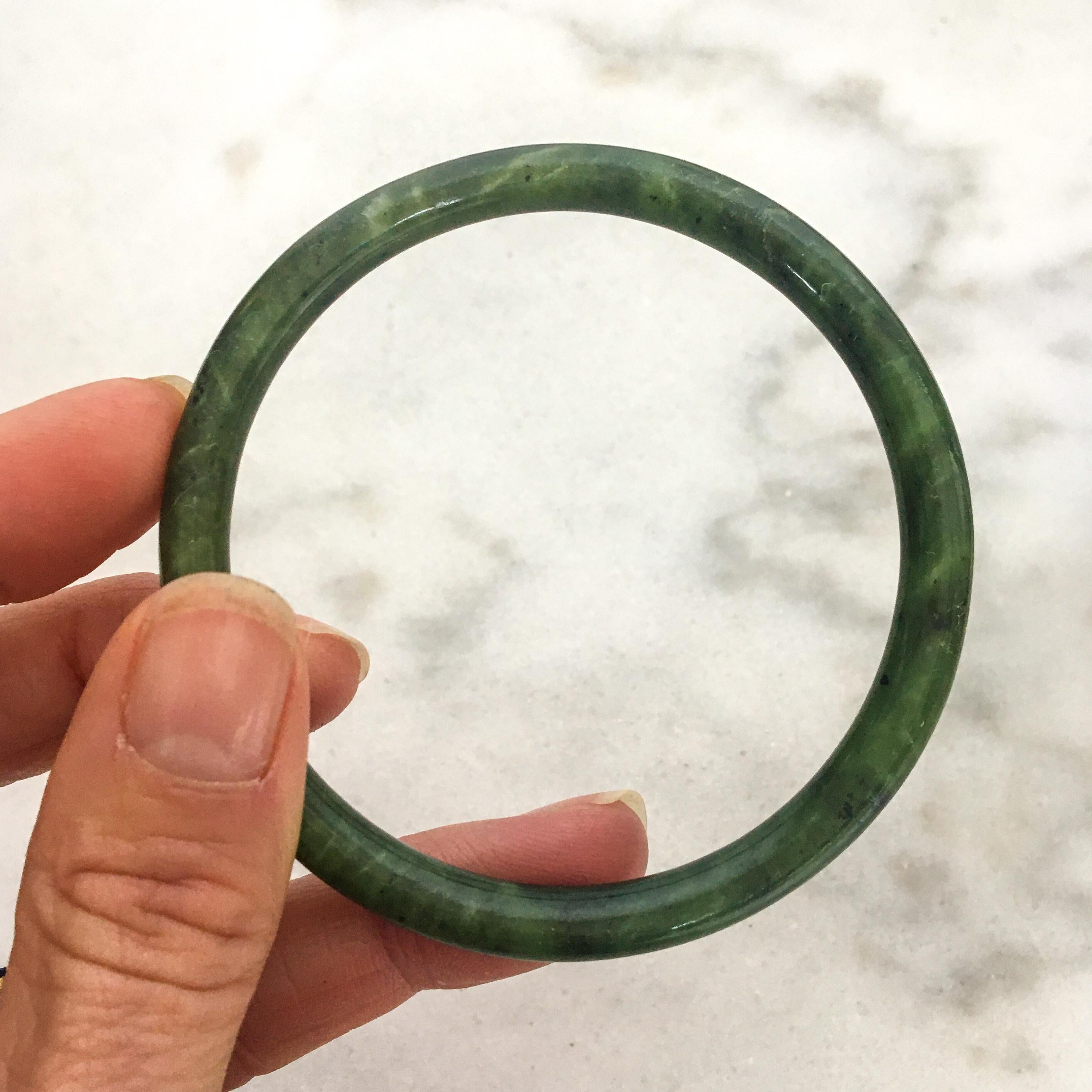 Dark green nephrite jade bangle bracelet made into a smooth round design. As a bangle requires a bigger piece of jade material, black spots that are commonly found are unavoidable. However, its good lustre and beautiful intense green more than