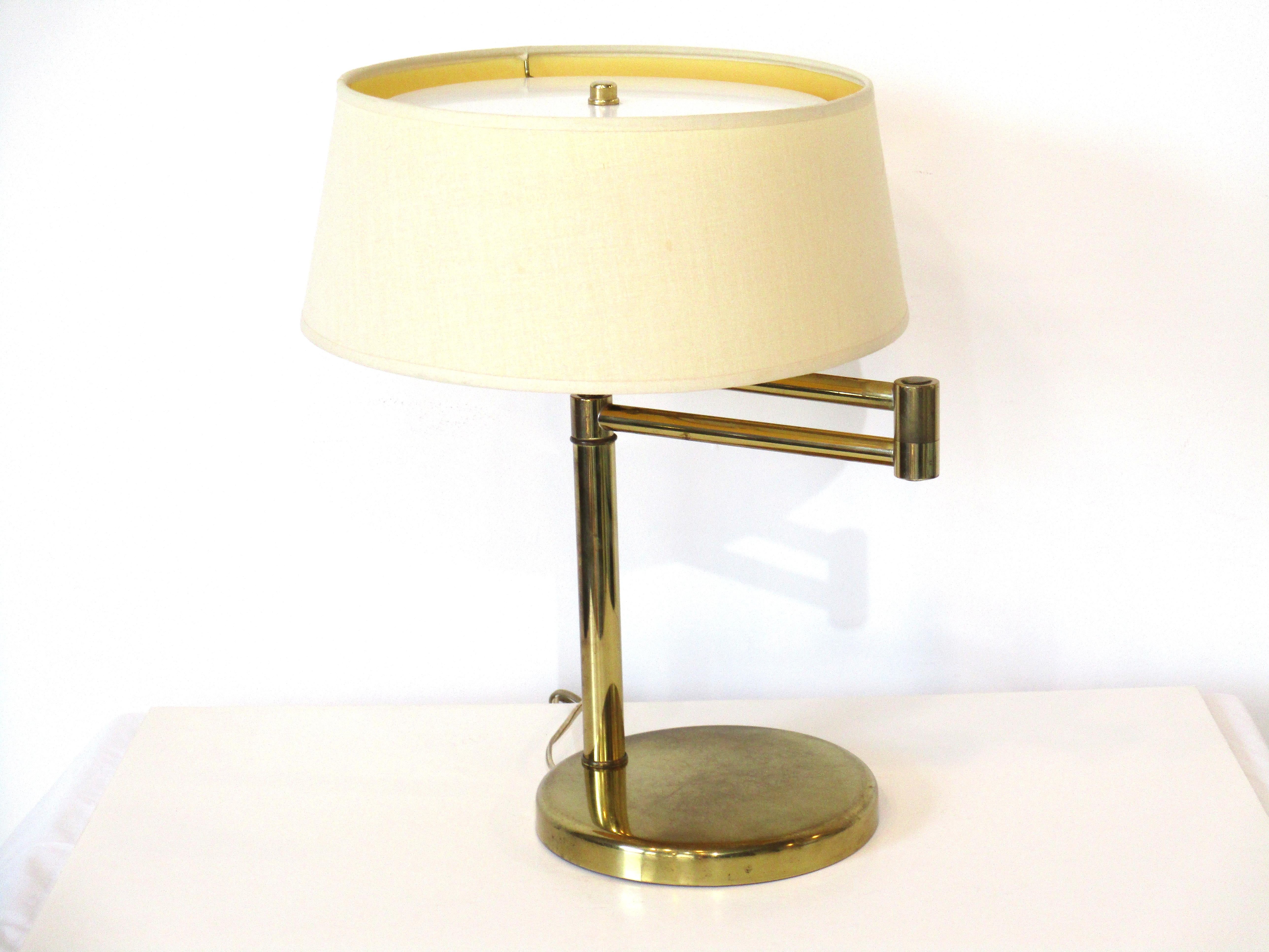 A brass swing arm table lamp by the Nessen Lighting company well known for their well crafted quality and the use of superior materials . Retains the original cream toned 14