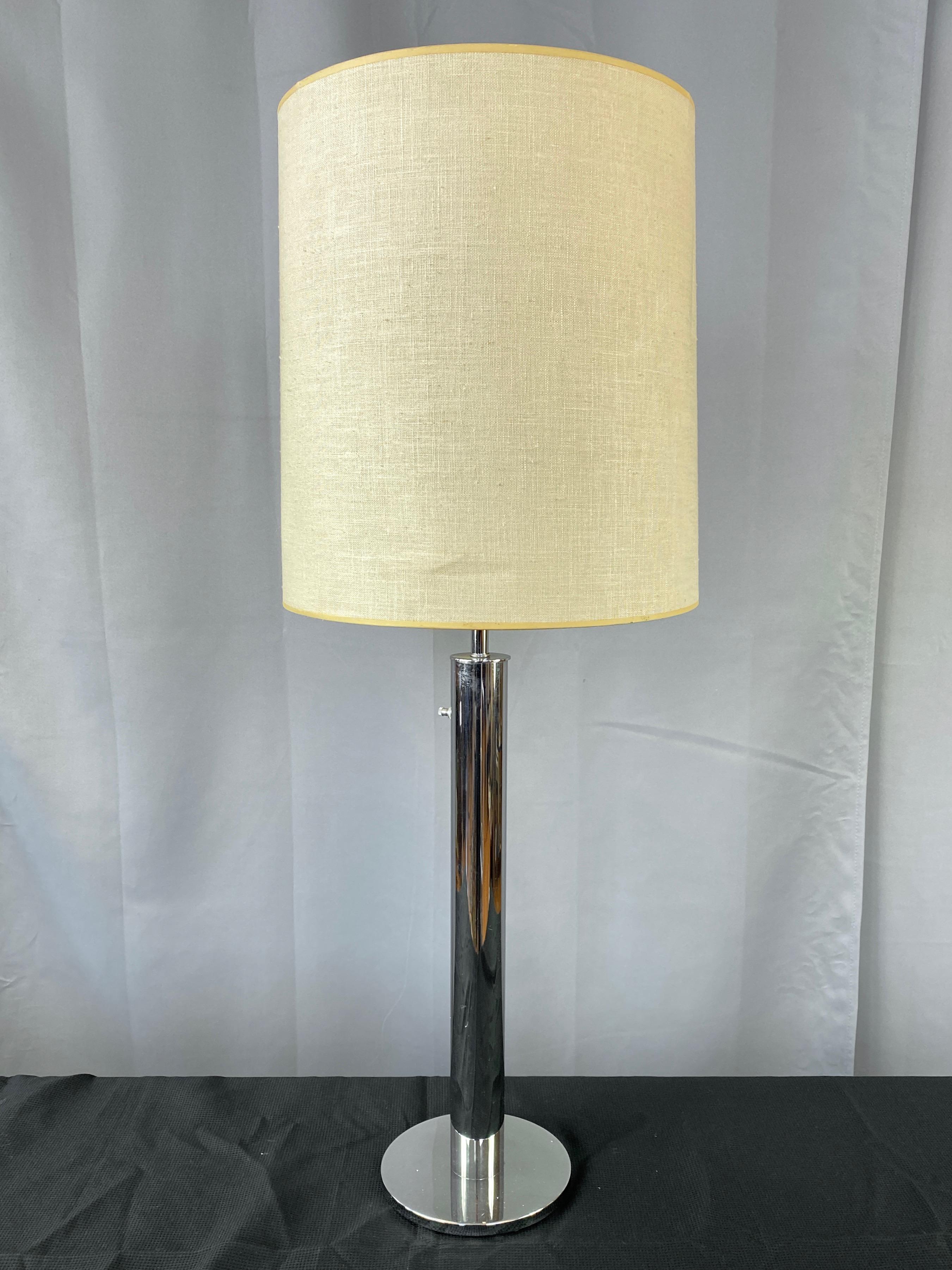 A circa 1970 tall minimalist chrome table lamp with original linen shade by Nessen Lamps, a successor to the highly influential Nessen Studios lighting design practice founded by Walter von Nessen and his wife Margaretta in 1927.

Sleek