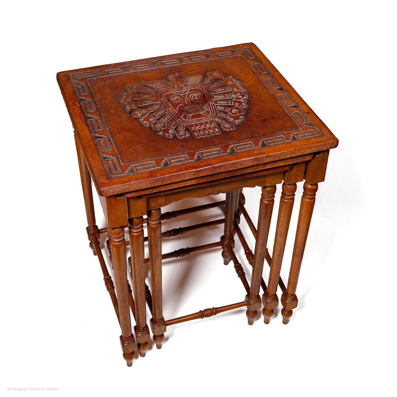 Three matching tables of decreasing size fitting inside each other all with embossed leather tops with stylized central motifs of Inca gods within geometric borders. The largest table with an embossed image of Inti the sun god,  the middle table