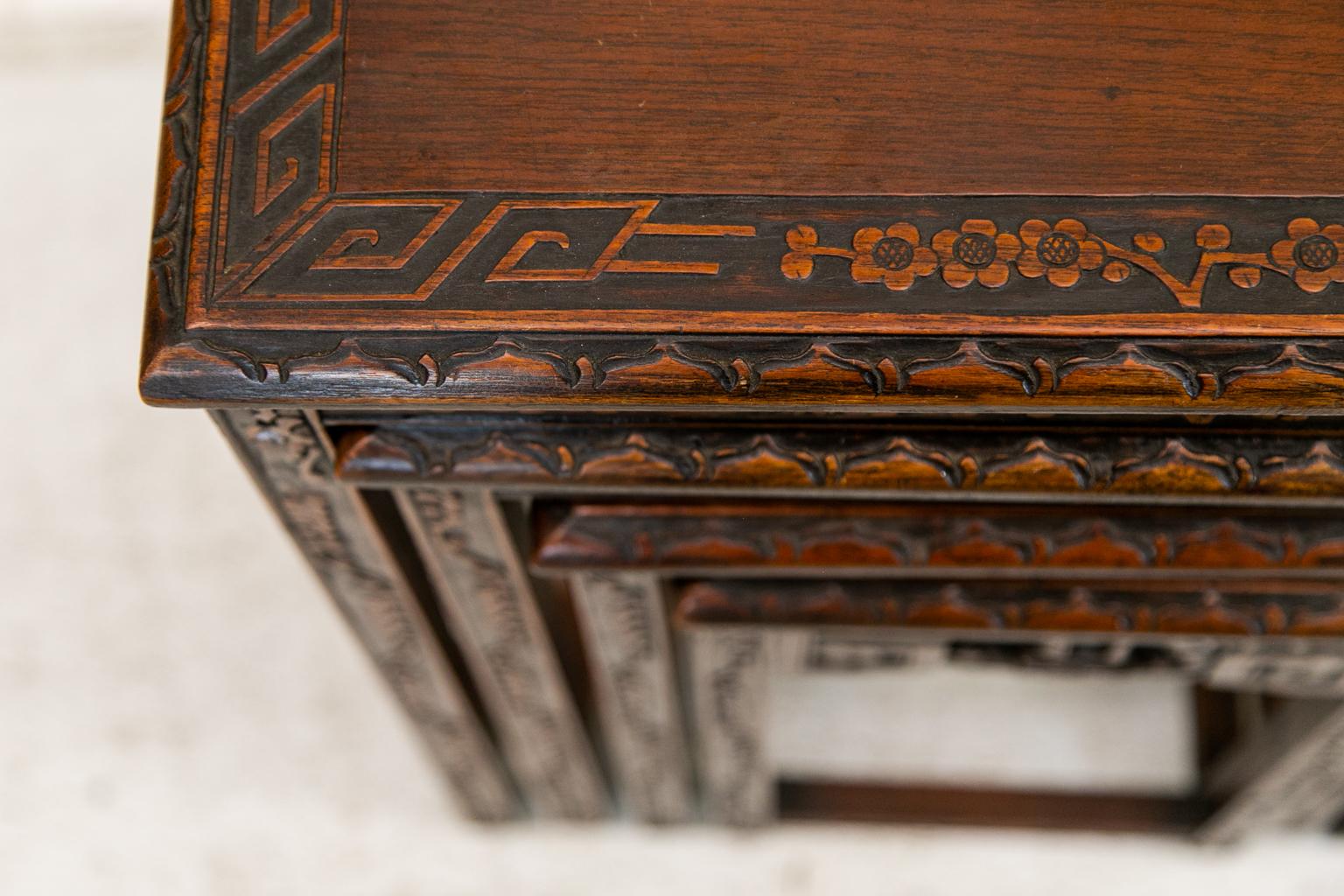 The tops of this nest of four Chinese teakwood tables are carved with geometric and floral motifs around the top borders. The smallest table has a carved central panel depicting trees and a boat. All tables are carved with the tree, sailboat panel,