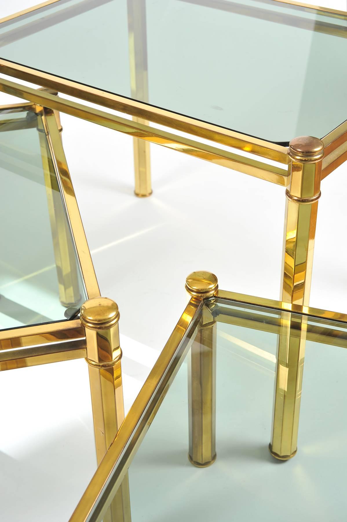 Nest of three Italian brass side tables with octagonal-planed legs. Each table inset with smoked glass top. Middle table measures 34cm high x 48cm wide x 31cm deep. Small table measures 27cm high x 41cm wide x 41cm  deep. Measurements for largest