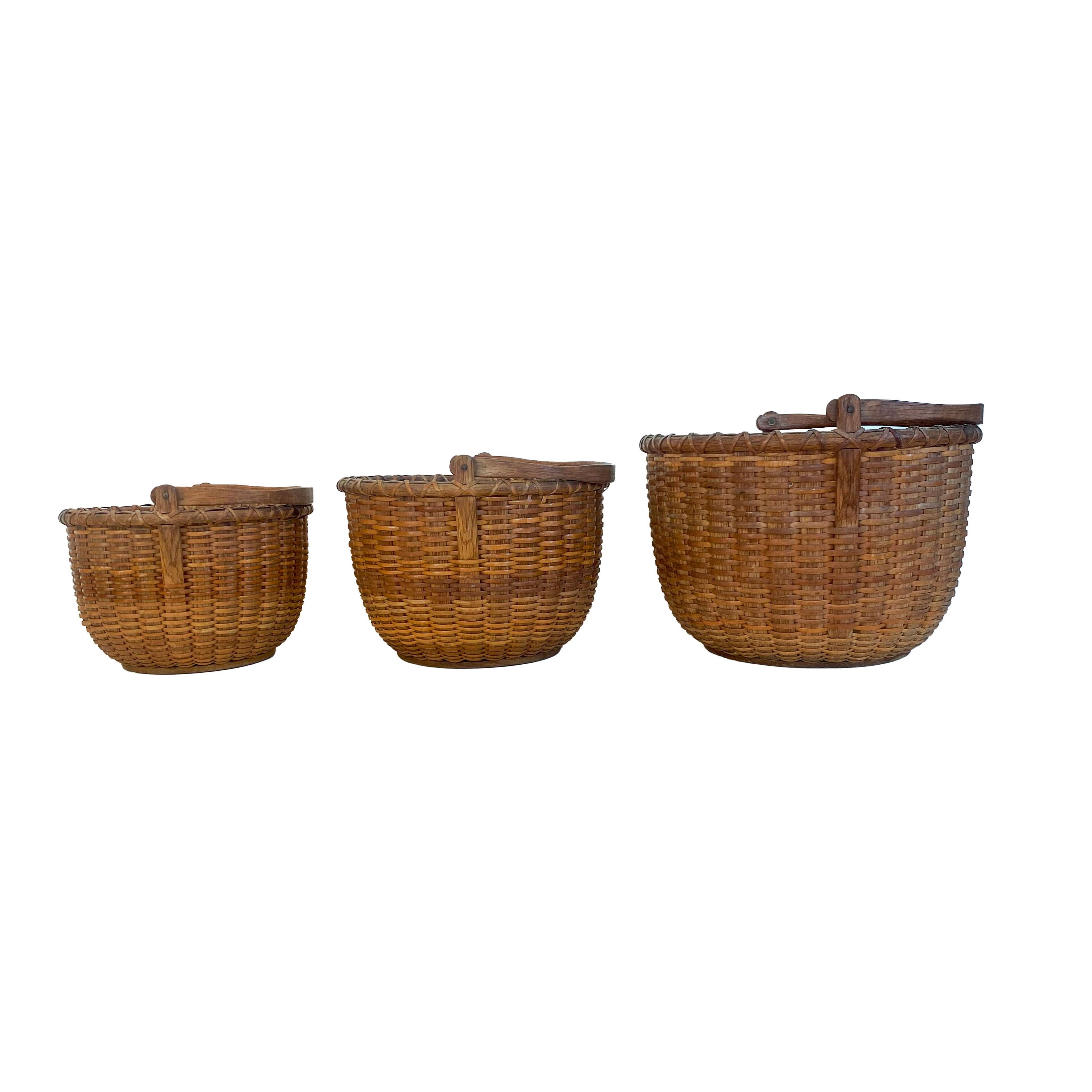 Nest of three Nantucket lightship baskets, the swing handles, staves and the ears ( which attach the handle to the basket) are all carved from oak. The bottoms are made from pine and each are stenciled with the maker's mark, 