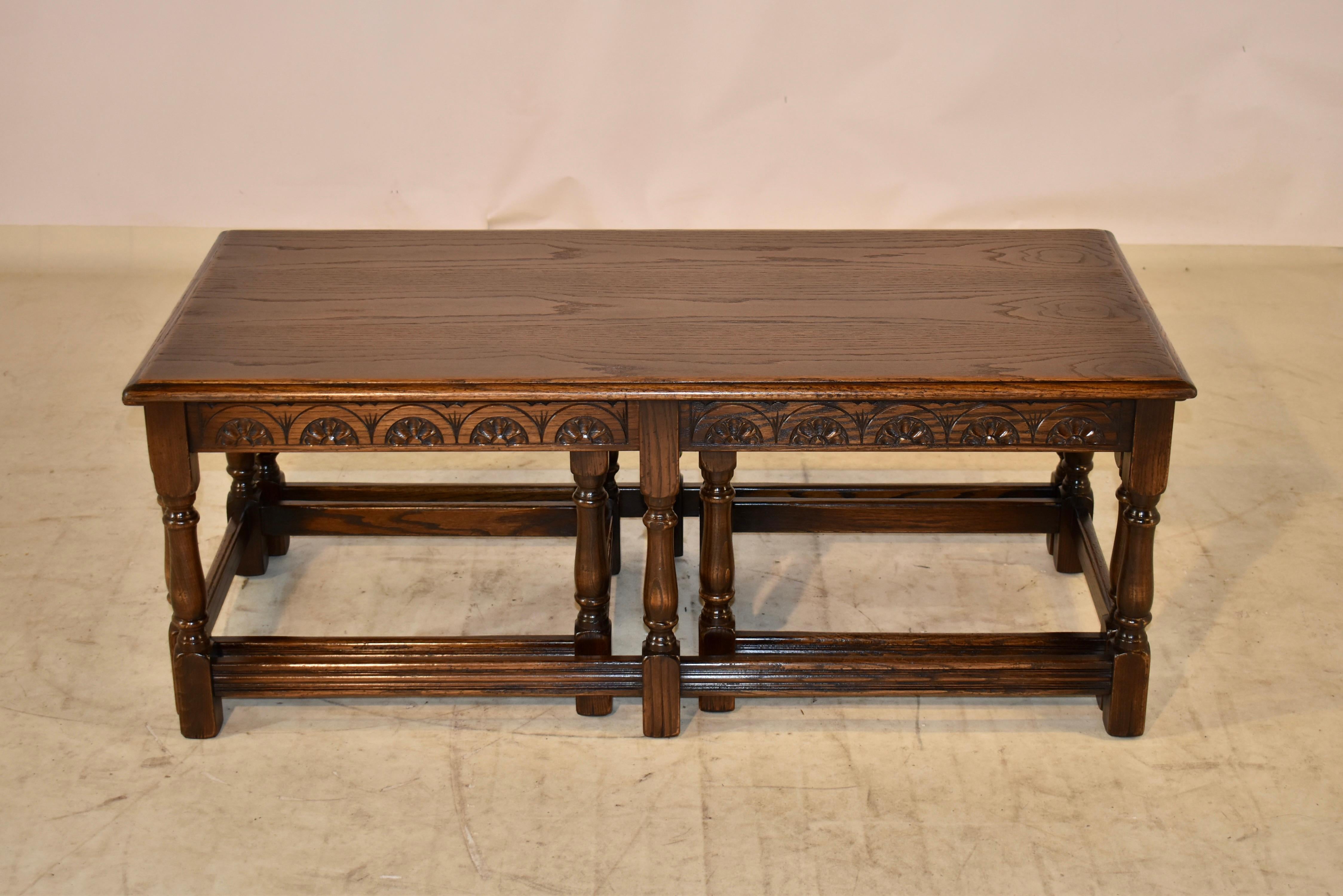 Set of three English nesting coffee tables made from oak. the top is beveled on all three of the tables, following down to a hand carved decorated apron on the largest table, and simple aprons on the smaller tables. The tables are supported on