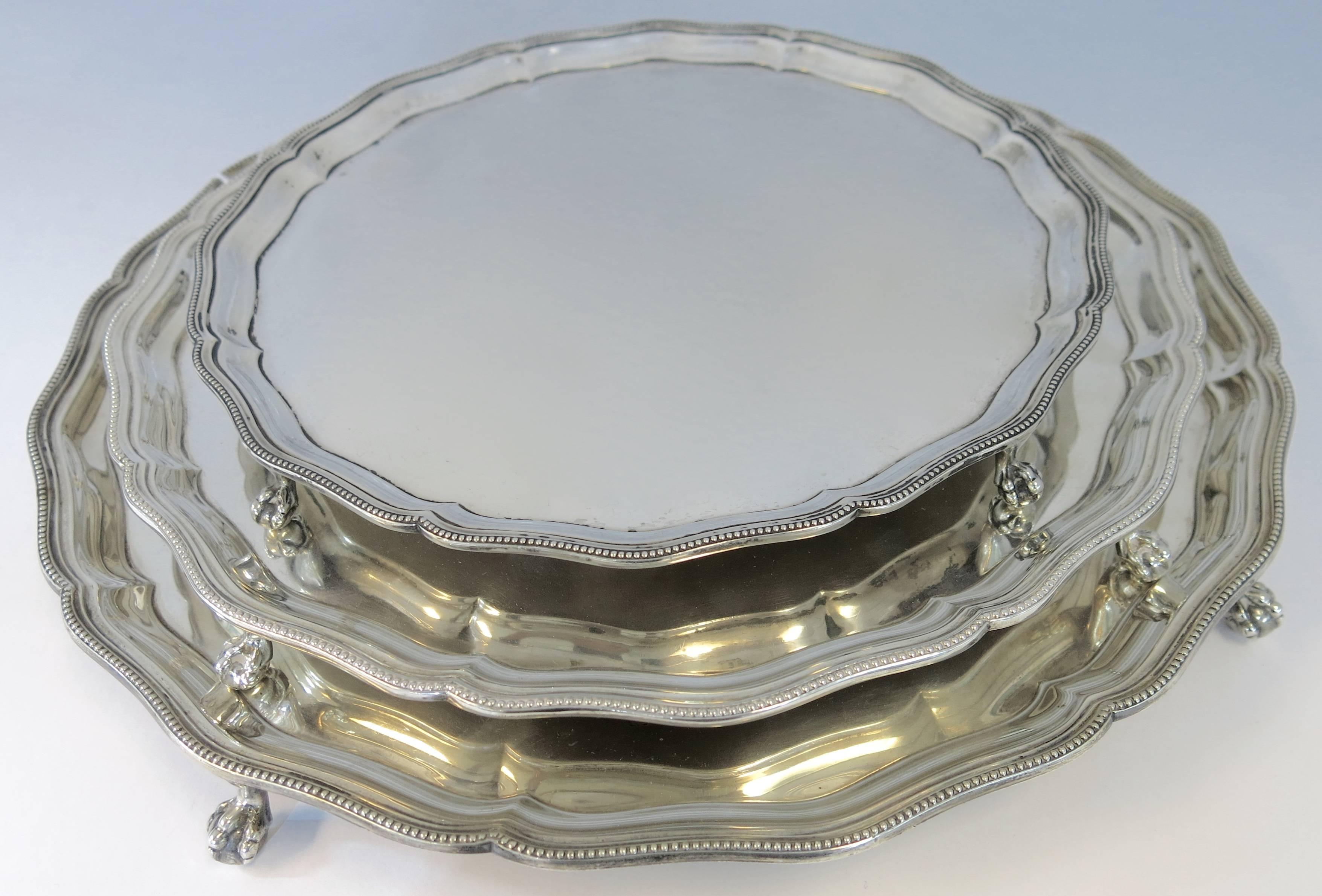 An unusual suite of three, nesting, sterling silver round footed salvers or trays made in England by Ellis Barker / Barker Brothers silversmiths. The three matching salvers are all with a fine bead or pearl applied border, and each stands on four