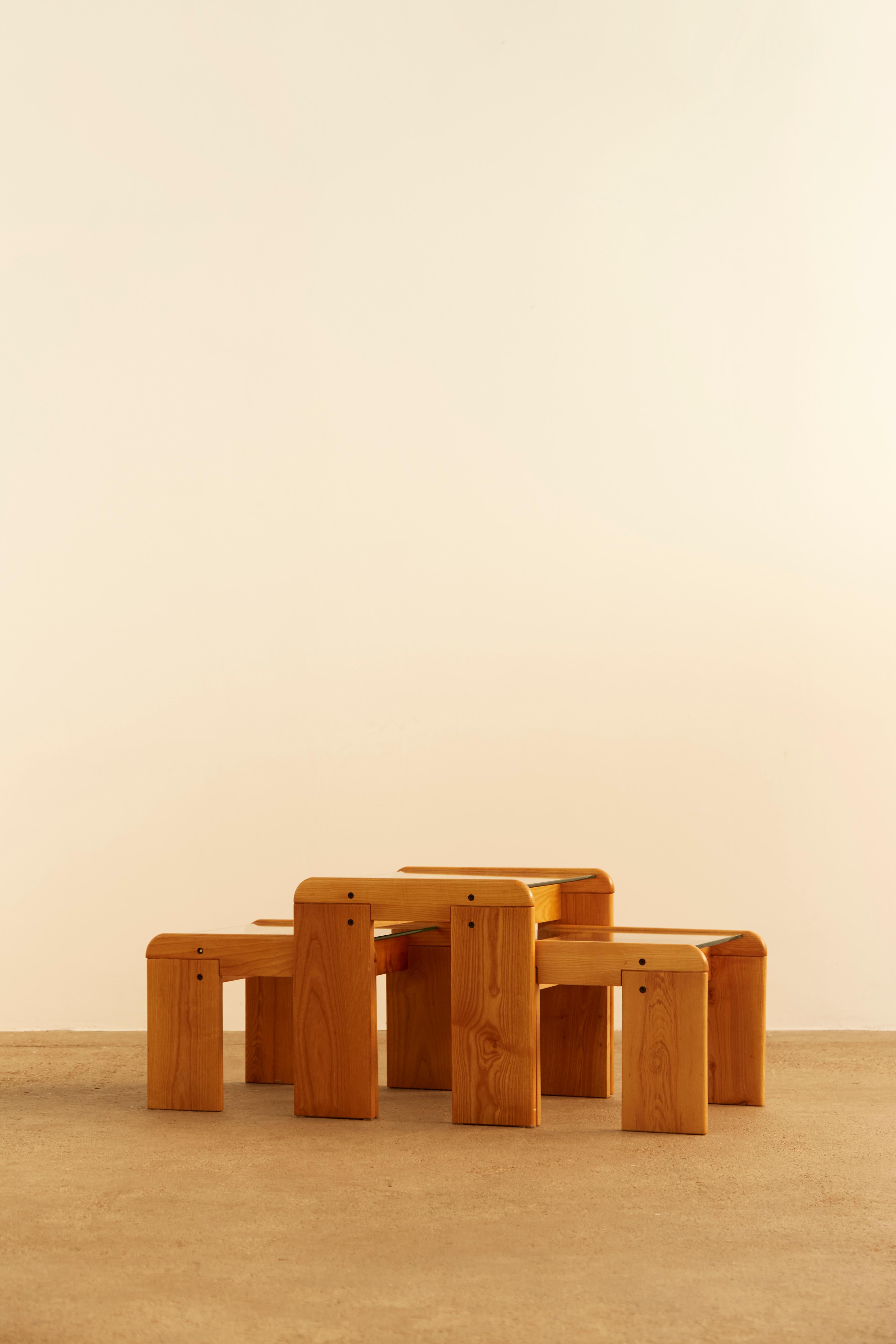 A set of three wooden nesting tables with a sculptural, minimalist design, crafted from warm-toned wood. Each table features rounded edges, visible joinery, and a smooth, natural grain that highlights its artisanal quality.