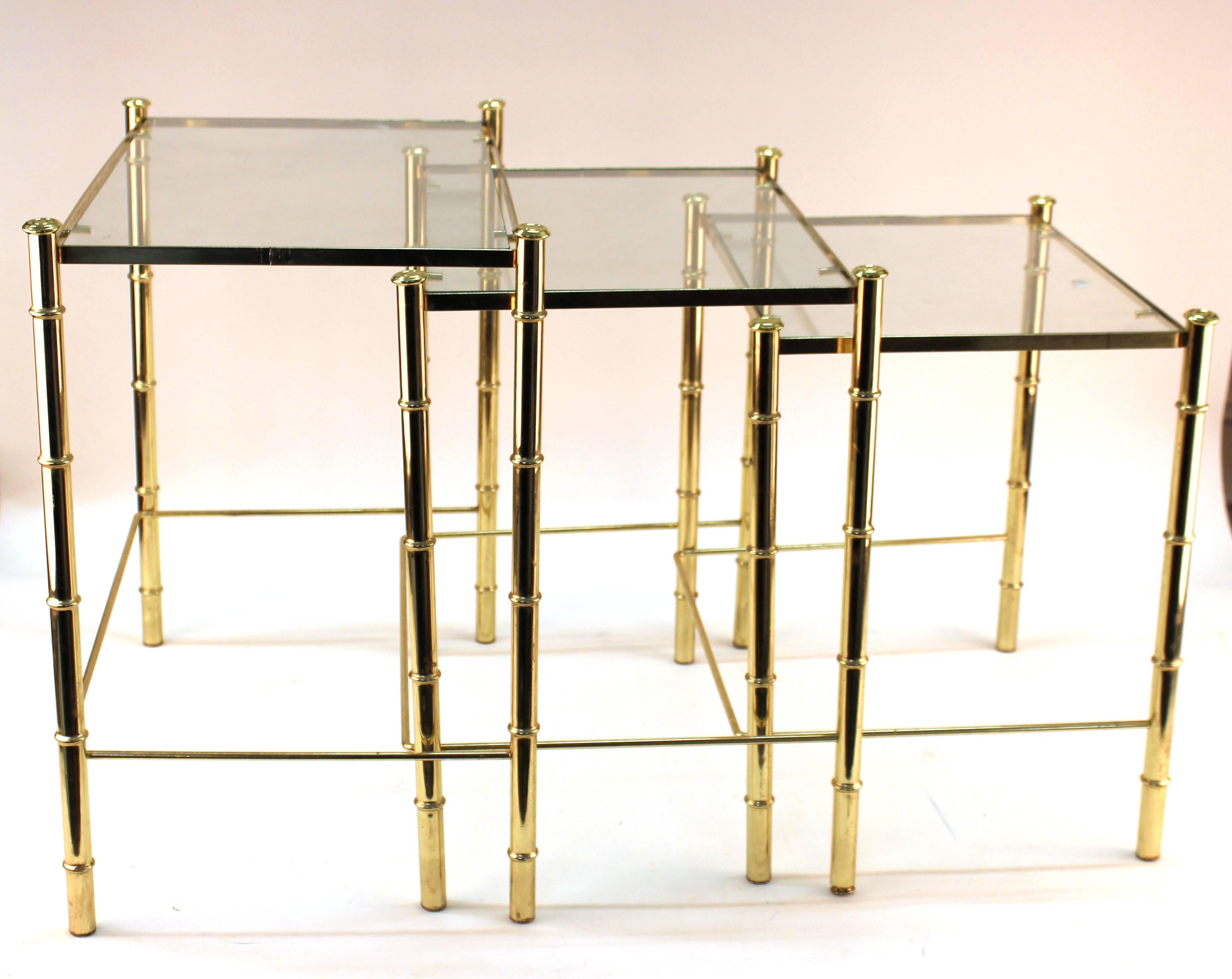 Nesting table and magazine holder set in gilt metal from France. Crafted with faux bamboo motif. Set includes three tables with gilt frames and glass tops. The magazine holder features a faux bamboo handle, criss cross pattern on sides and faux