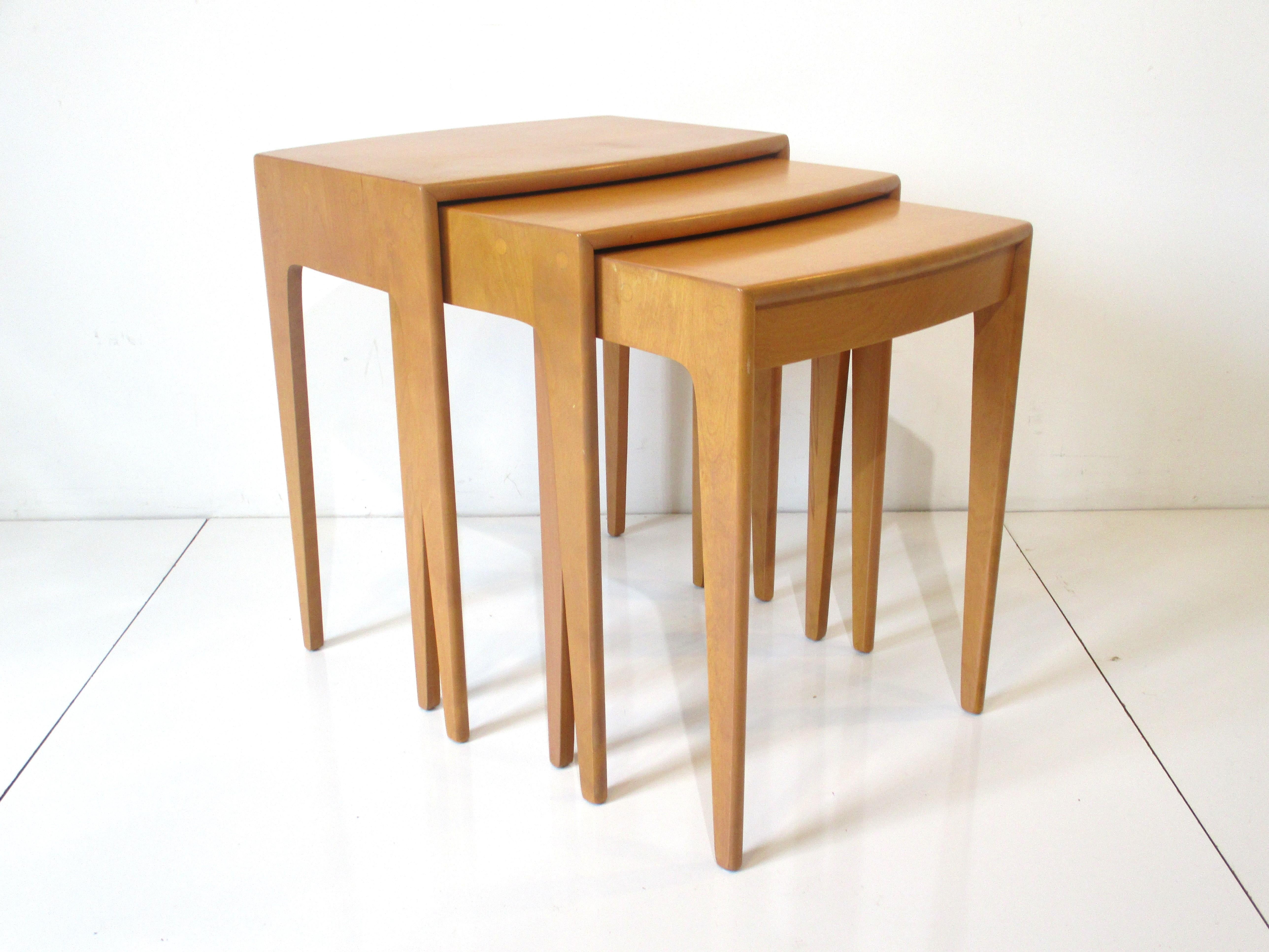 A set of three well crafted nesting tables with curved front top edges and tapered legs when nested have a great design aesthetic . Made of solid maple wood and has the original champagne finish designed by Leo Jiranek and Ernest Herrmann for the