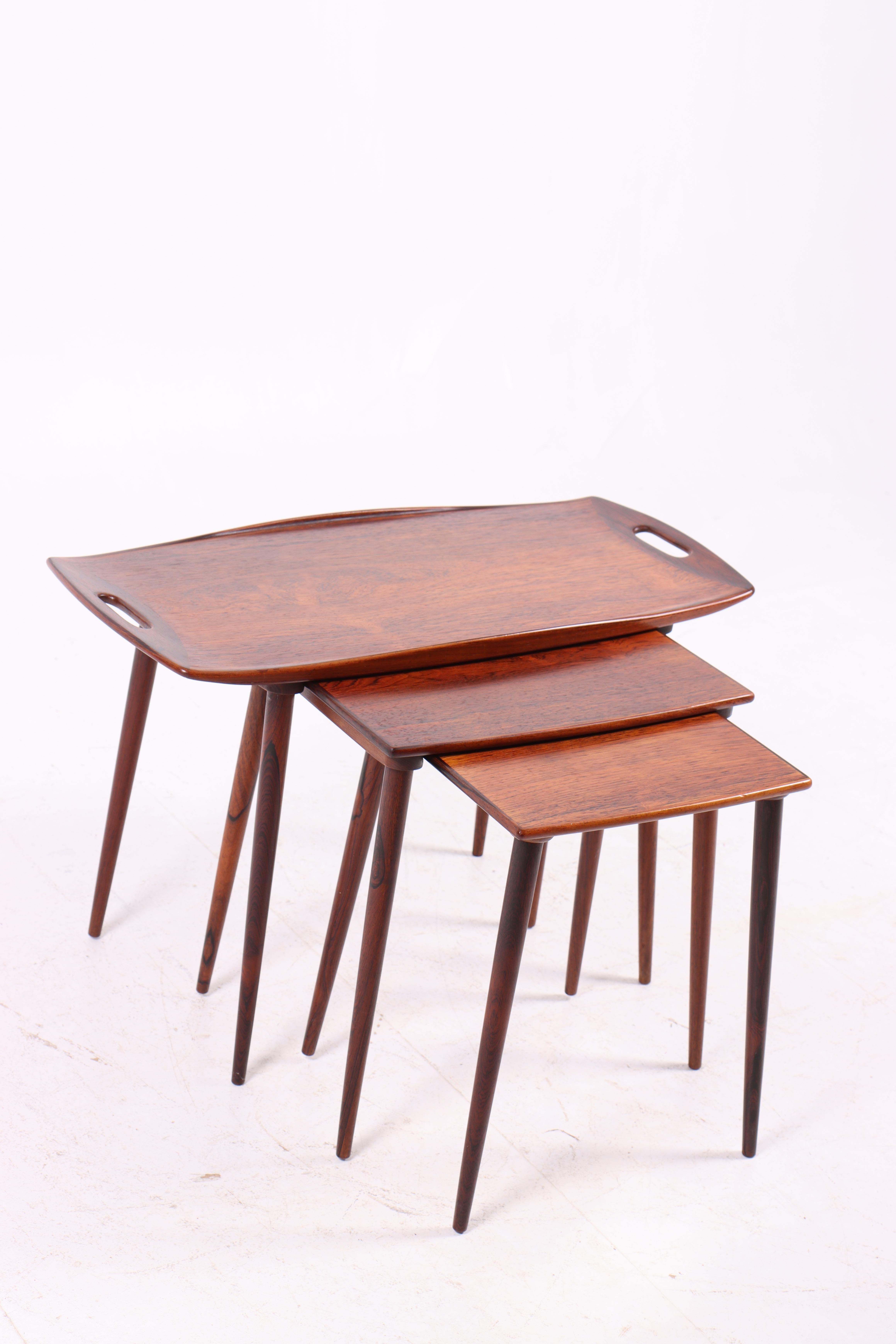 Conjunto de elegantes mesas nido de madera de palisandro con patas de palisandro macizo. Los tableros presentan un diseño limpio y sencillo, que confiere al conjunto una expresión pura y atemporal. La mesa más grande está provista de asas laterales,
