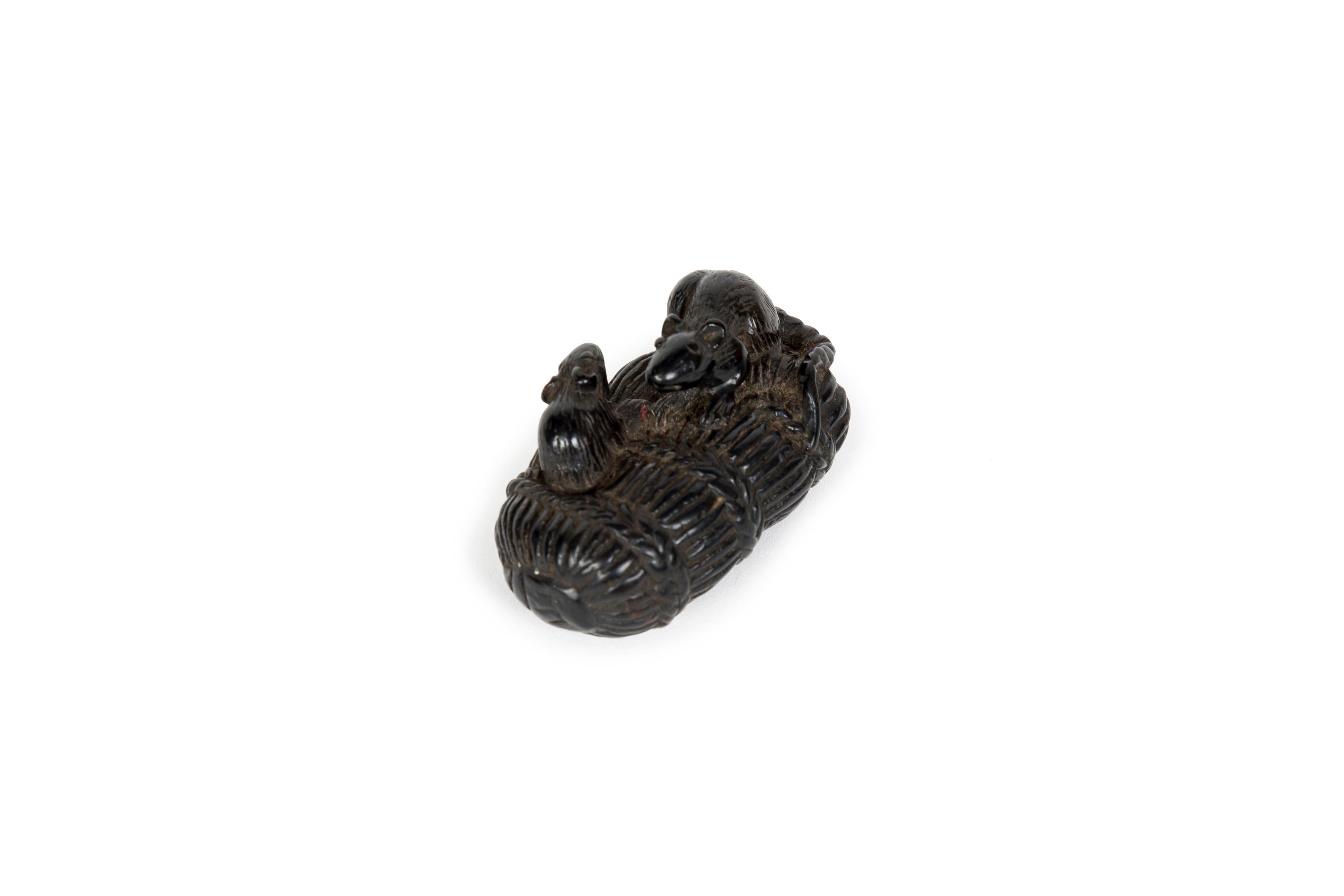 Netsuke, très probablement en bois d'ébène, représentant deux souris sur une vannerie, l'une s'en extrayant et l'autre reposant dessus. Traitement réaliste du pelage et de la queue ainsi que du motif de tressage de la vannerie. Malgré sa mauvaise