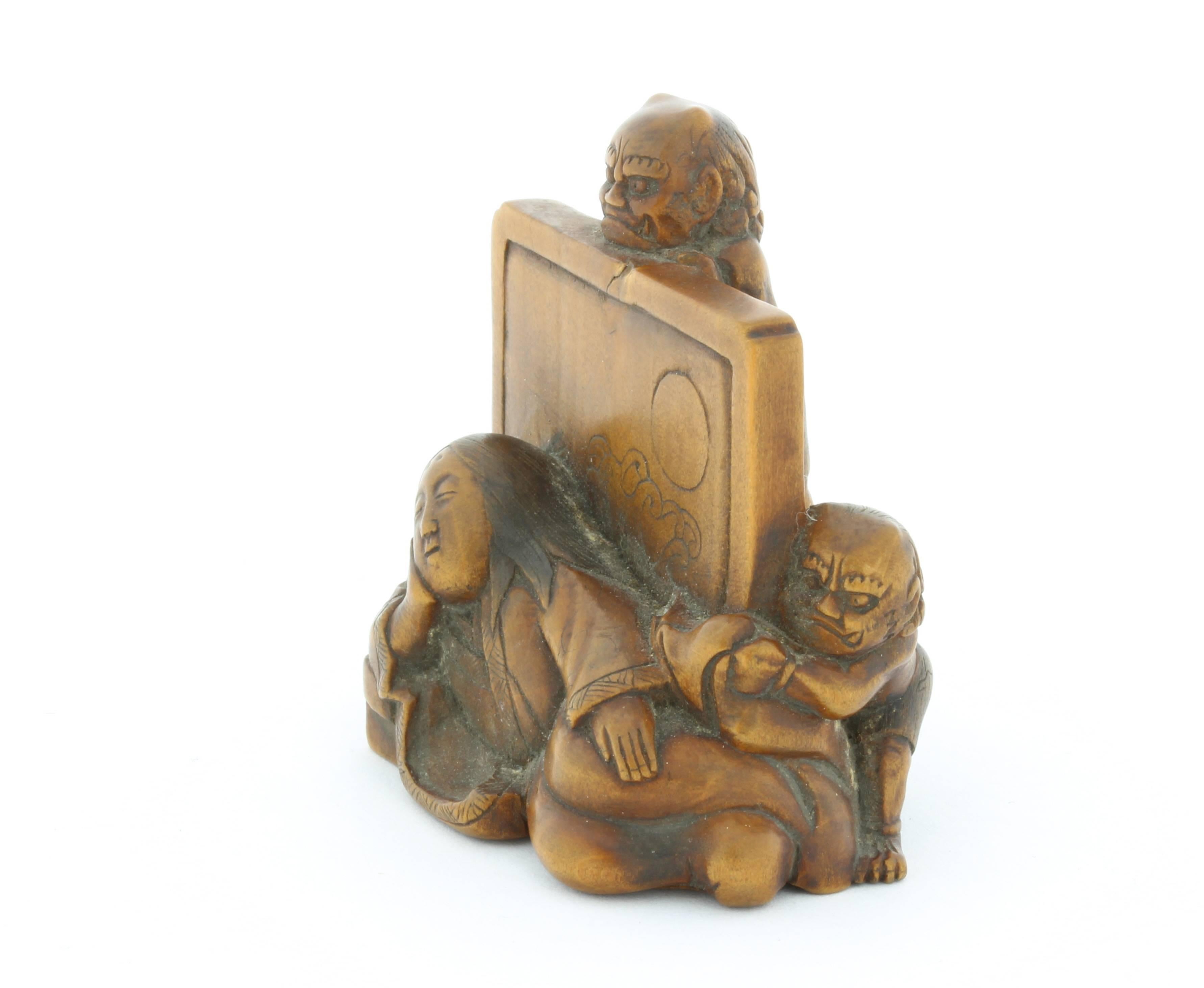 This netsuke is made entirely out of wood and depicts a sleeping lady being watched by two oni (demons). Her long hair is loose and her eyebrows are carved high above on her forehead, suggesting her noble background. The screen behind her shows a
