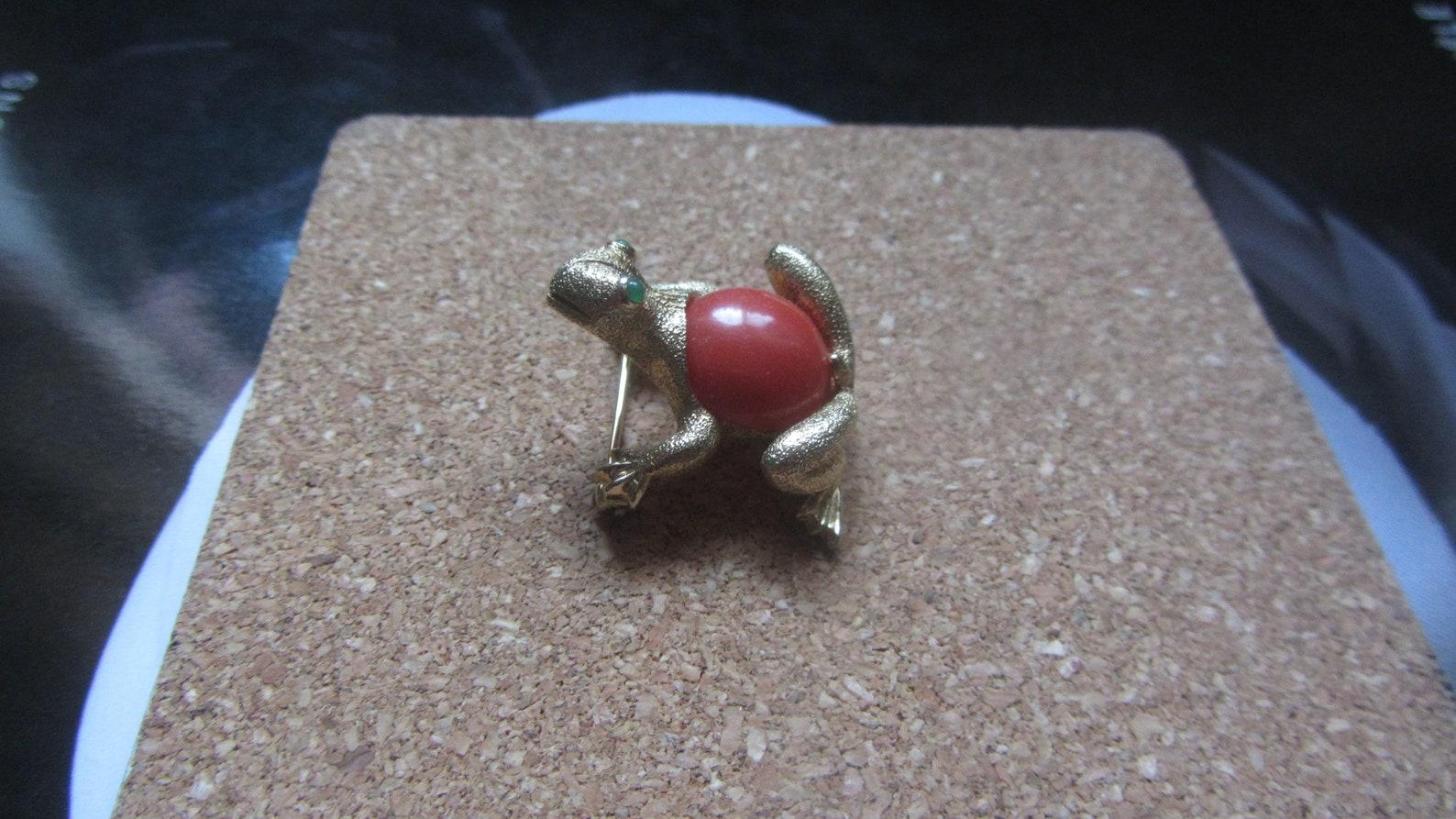 Vintage Nettie Rosenstein frog brooch. Gold tone textured metal. Marbled faux coral cabochon. Tiny green glass eyes.

Markings: Nettie Rosenstein in script

Circa 1950s
Closure: roll over C-clasp
Excellent Condition

✂-----Measurements

Brooch: 1