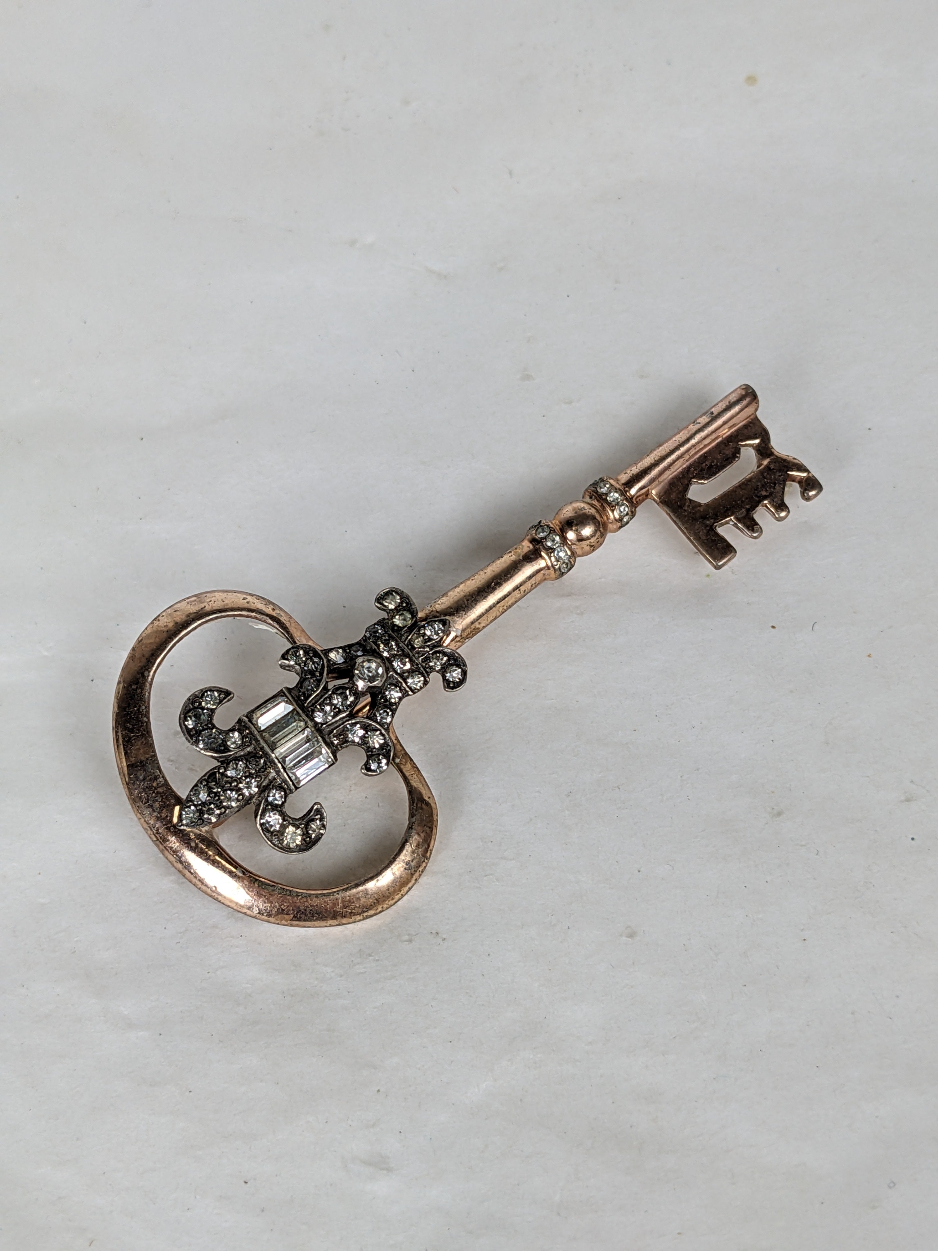 Nettie Rosenstein key brooch circa 1940s of rose gold plated sterling silver, decorated with a rhodium plated sterling Fleur de Lis motif of crystal baguettes and rhinestone pave.  Excellent Condition, Signed Nettie Rosenstein , Sterling. L  3