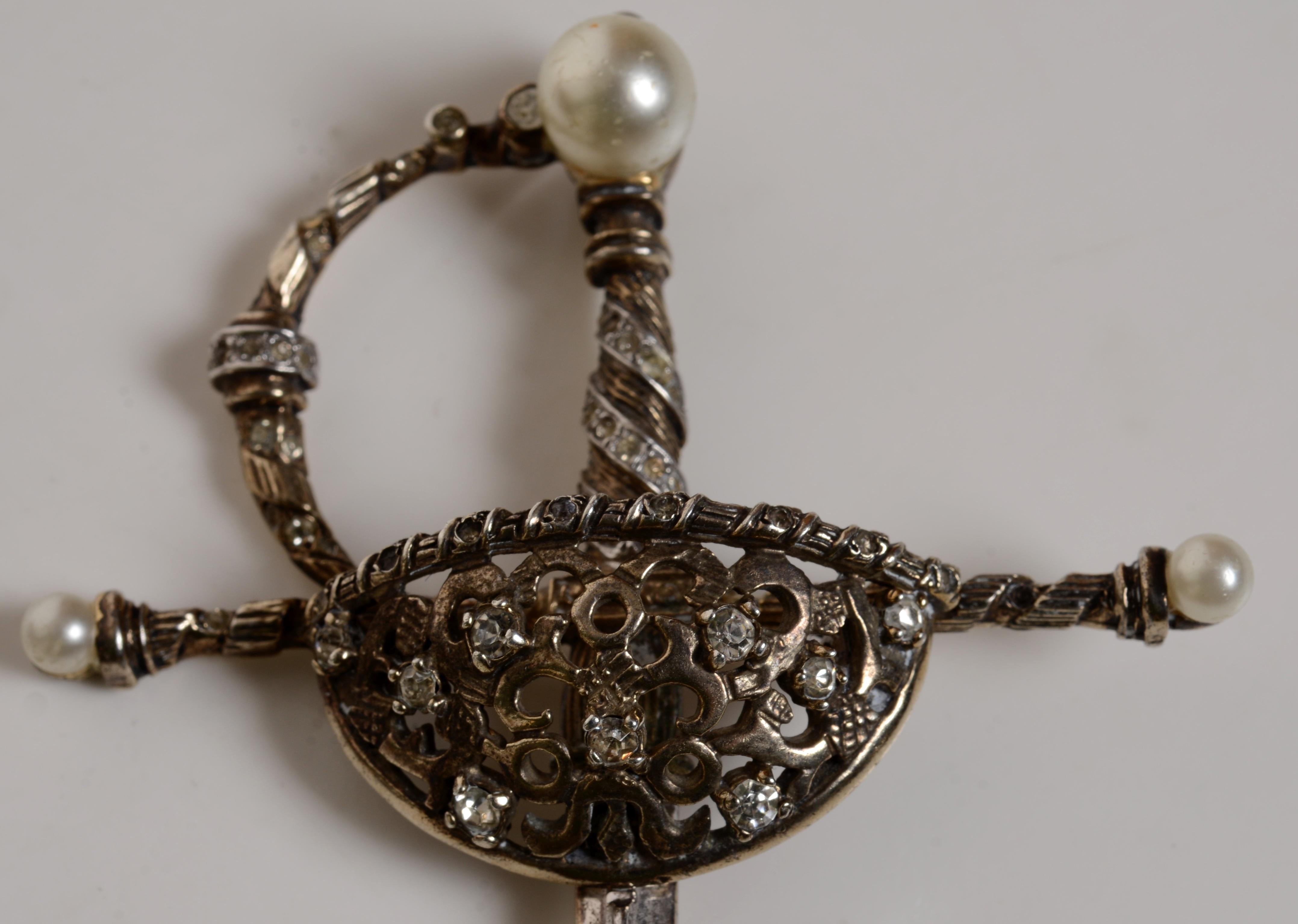 Spilla a forma di spada in argento di Nettie Rosenstein con perle finte e strass. L'elaborato paramano con lavorazione a giorno e strass. Il Quillon e il paraschiena con montature ritorte e terminali in finta perla. Nettie Rosenstein (1890 - 13