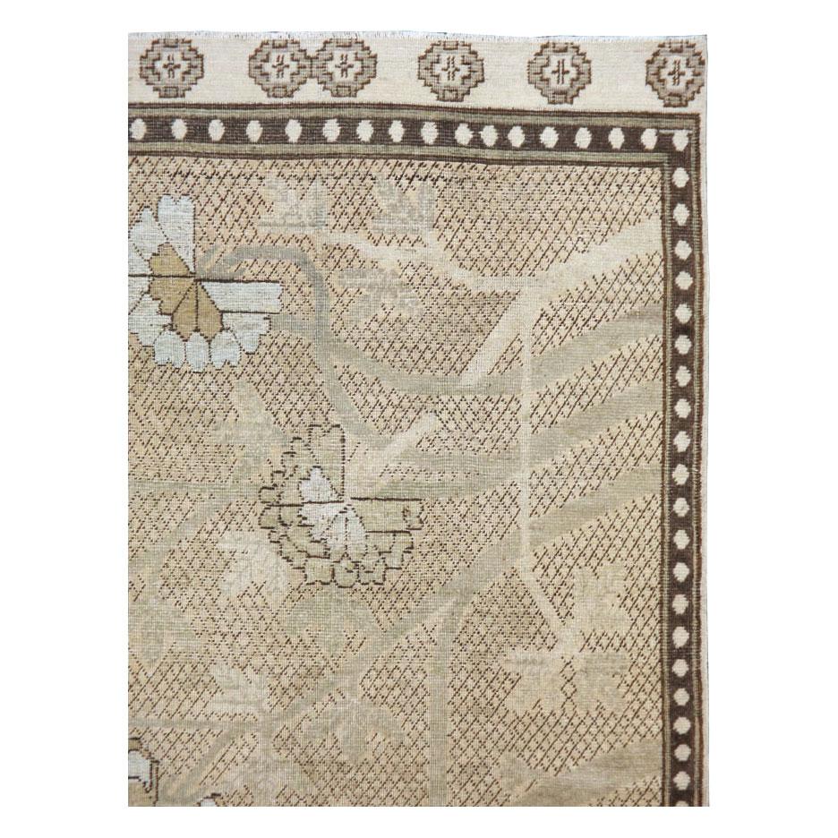 An antique East Turkestan Khotan accent rug in gallery size format handmade during the early 20th century. The beige field consists of a calming brown diamond lattice pattern with a peony tree drawn on top. The peony tree is made up of a palette in