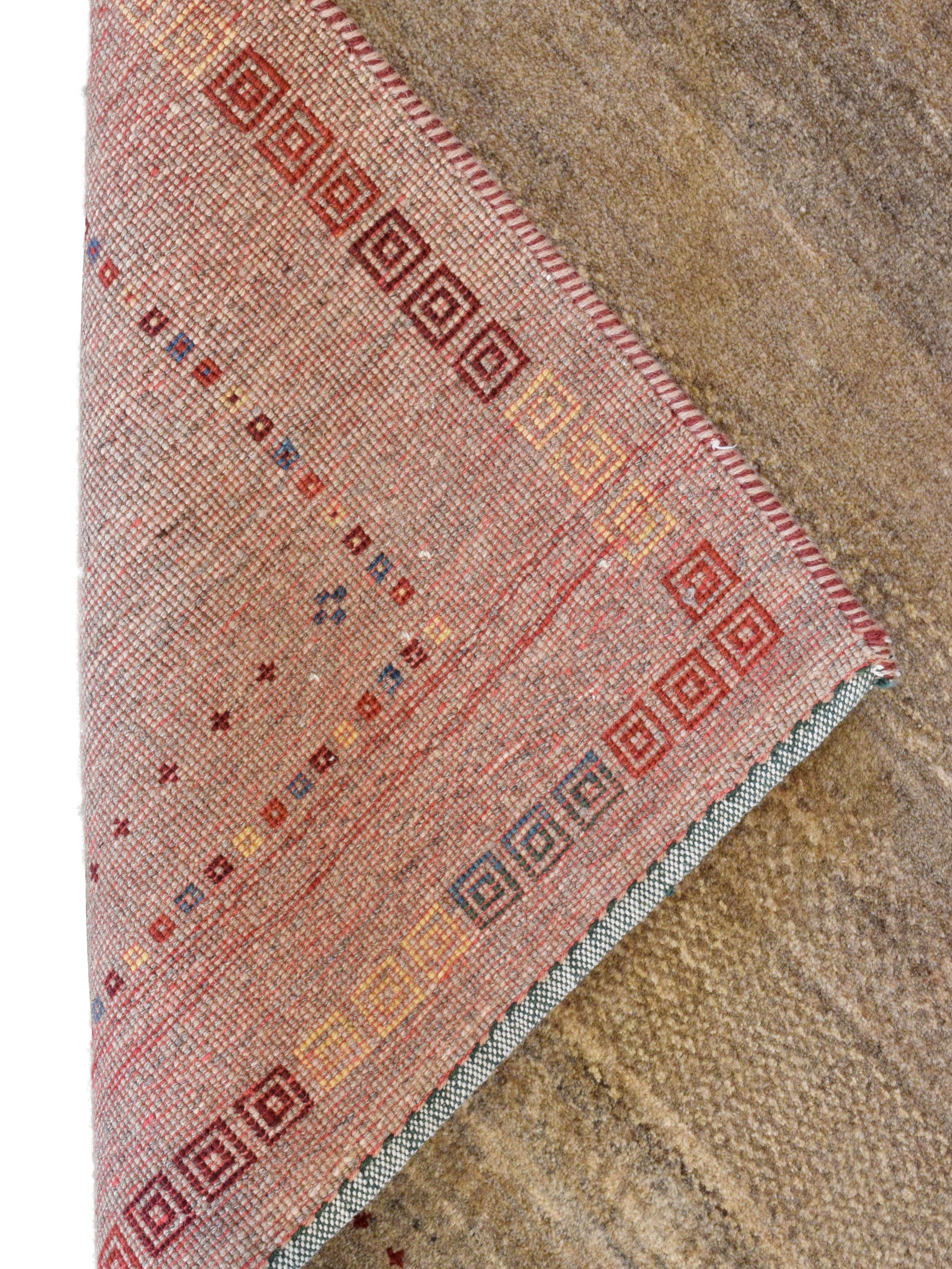 Striking tones of taupe, gold, red, blue, and orange highlight the splendidly striated field of this neutral brown Persian Gabbeh area rug in wool that measures approximately 4' x 7'. The abrash of this design provides the simplistic background with