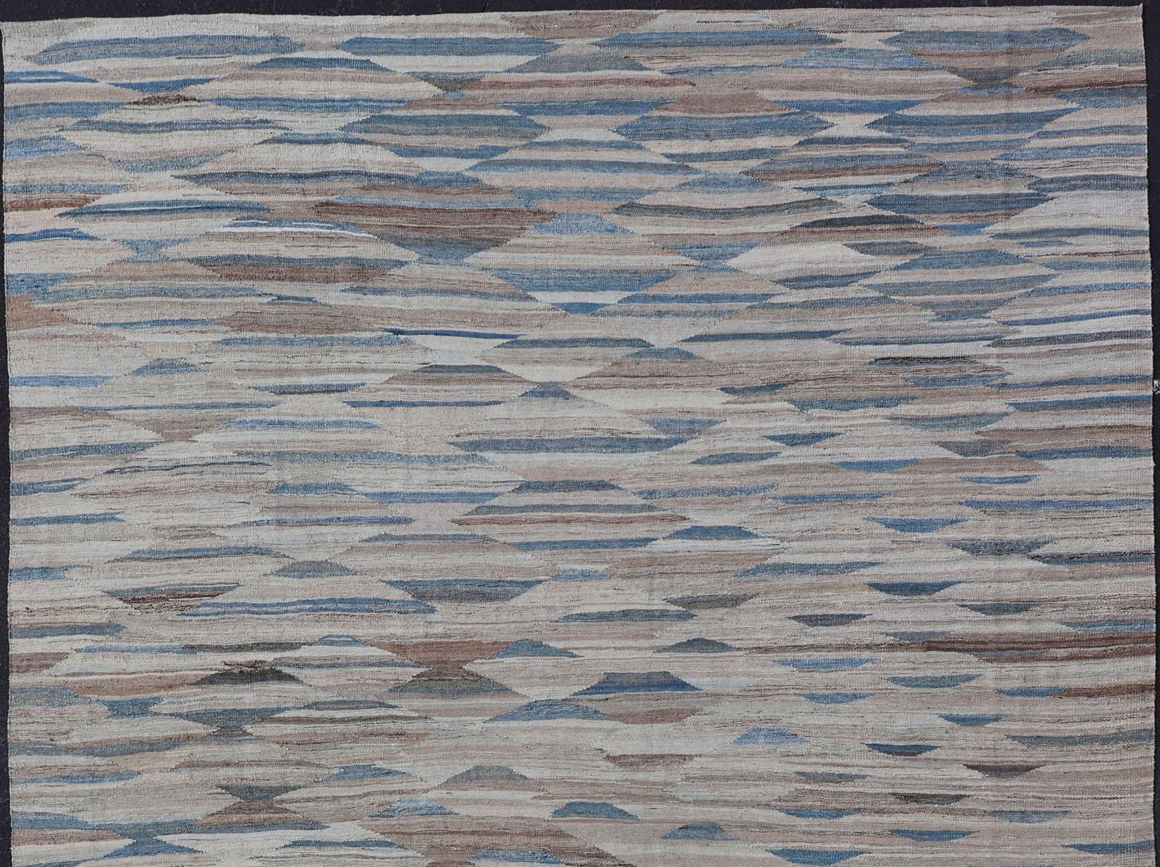 Kilim moderne avec motif géométrique en  variation de tons bleus, bruns, bronzés et neutres. 

Grand tapis Kilim moderne et décontracté, tissé à plat en Afghanistan, dans des variations de couleurs bleu, marron, tan et crème. Tapis Keivan Woven Arts