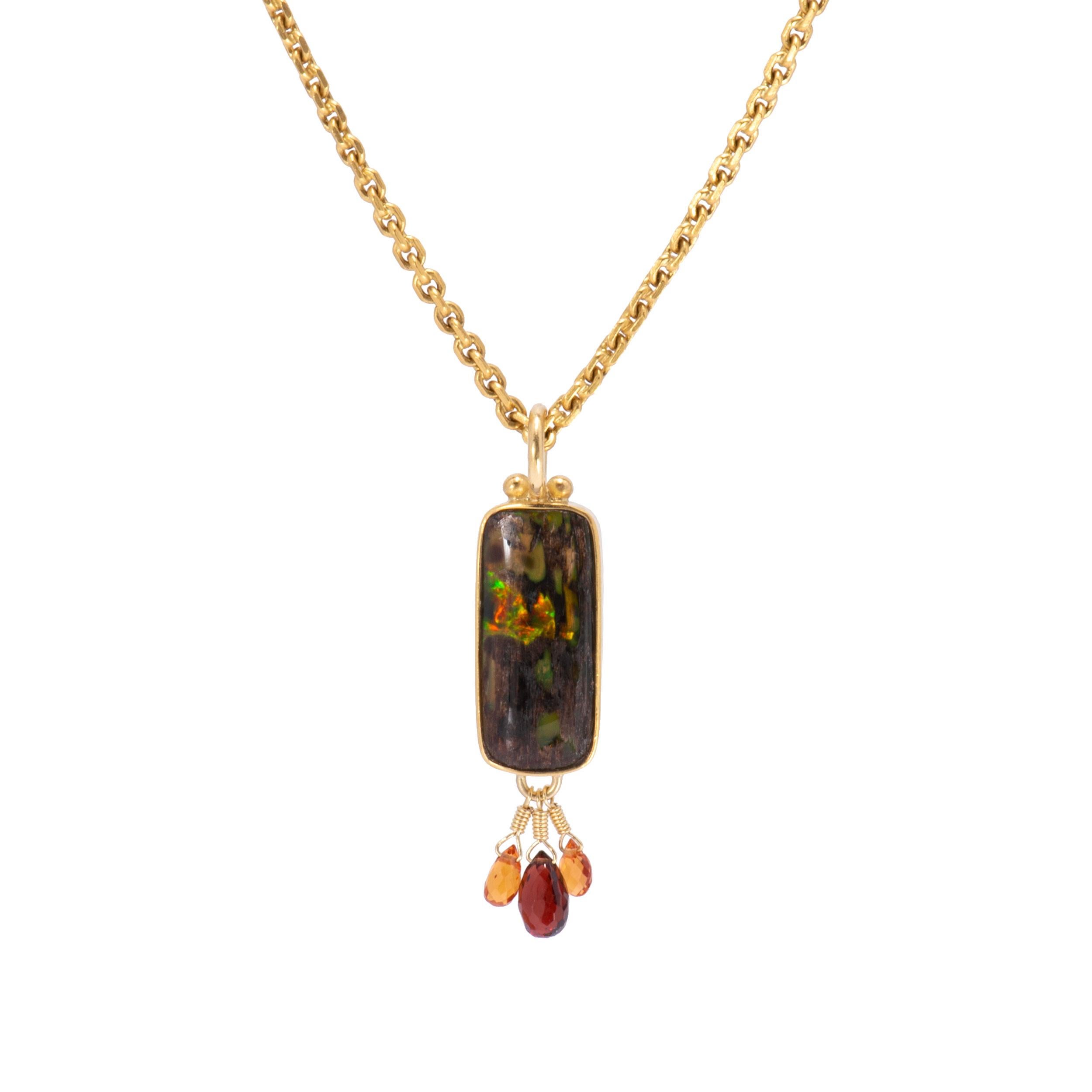 A lozenge pendant of Nevada Wood Opal gleams with green, orange, red and milky gold lights from the depths and is tipped with red garnet and orange sapphire briolettes. Bezel set and beaded in 22k gold and finished with an 18k gold bail and