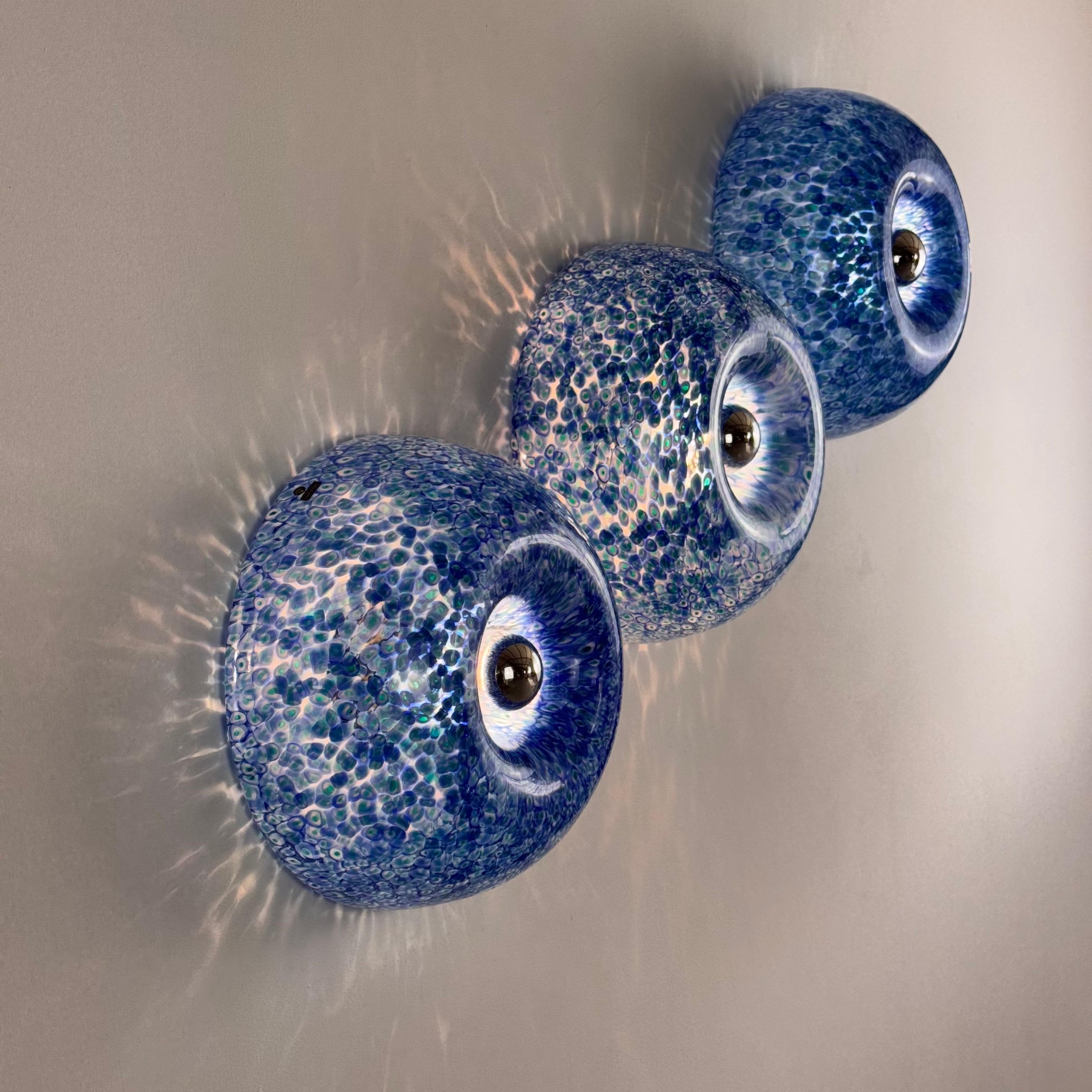 A highly decorative wall or ceiling light designed by Gae Aulenti in the 1970s for Vetrerie Vistosi, as part of the expressive ‘Neverrino’ series. Crafted in hand-blown Murano glass with blue murrine and shimmering green reflections, each light is a