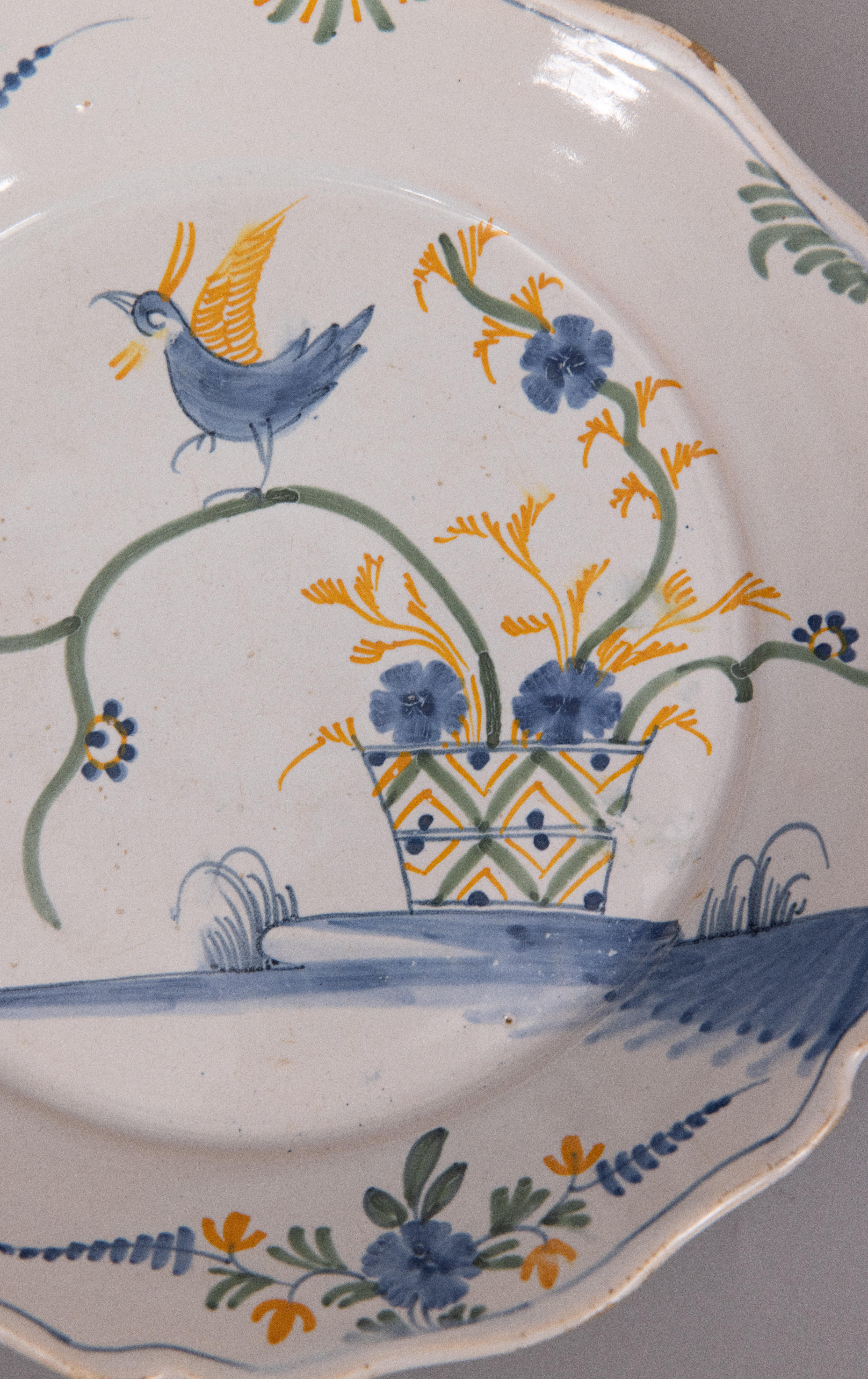 A wonderful 18th century Nevers polychrome plate feauturing a bird perched on top of of a spray of flowers emerging from a painted flower pot. Hand painted in vibrant blue, yellow, and green with swags on the border of the scalloped rim.