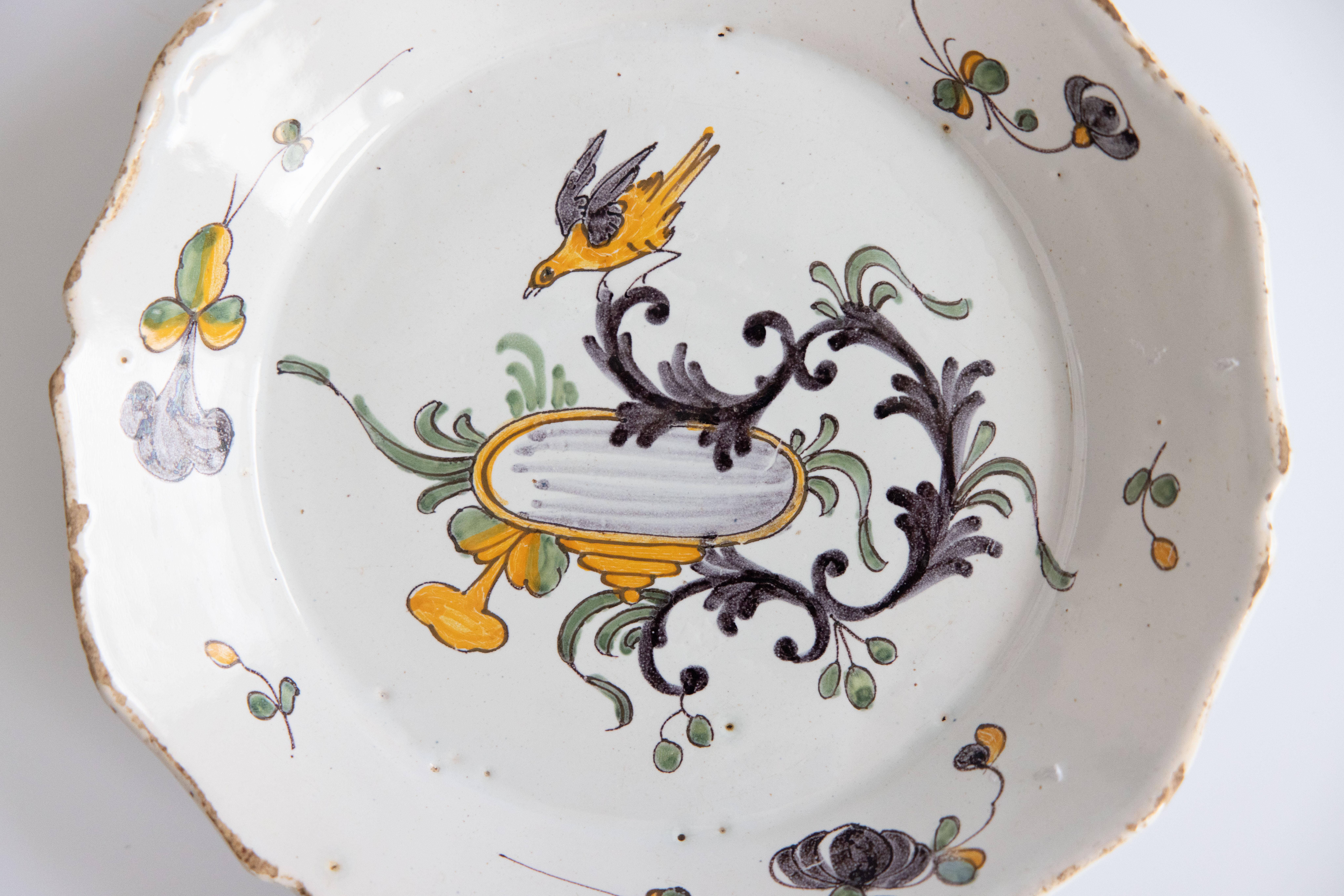 Maravilloso plato policromo de Nevers del siglo XVIII que representa un pájaro cantor posado sobre una enredadera rastrera, mirando hacia abajo sobre una pileta para pájaros; el borde está decorado con flores. Pintada a mano en vibrantes tonos
